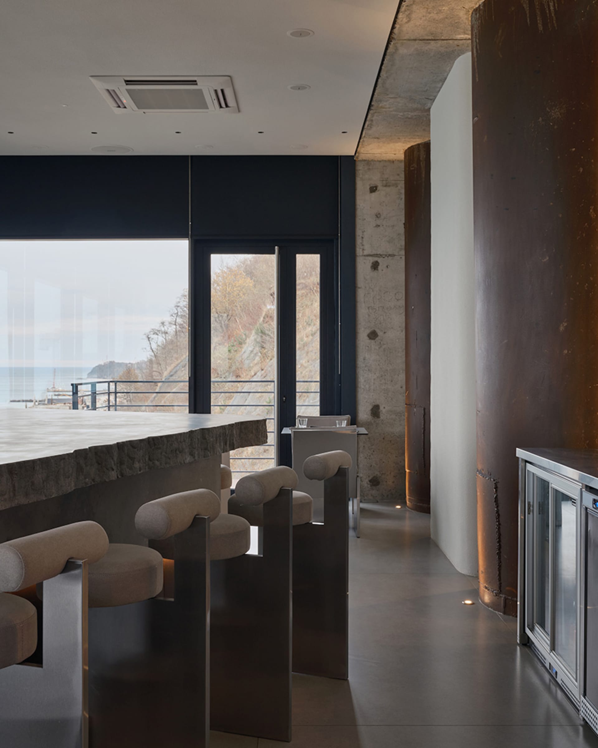 Open living area with a modern bar, chairs, a dining table, a couch, and a TV, set in a contemporary space with clean lines and minimal decoration