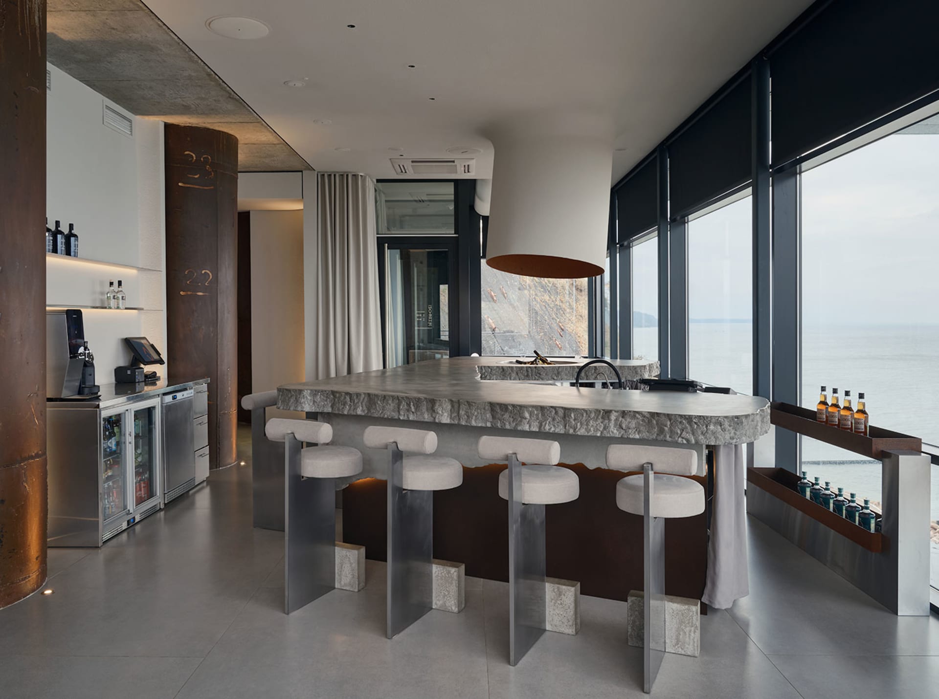 Open modern kitchen and dining area with a large island, stools, dining table, chairs, and natural light from a large window