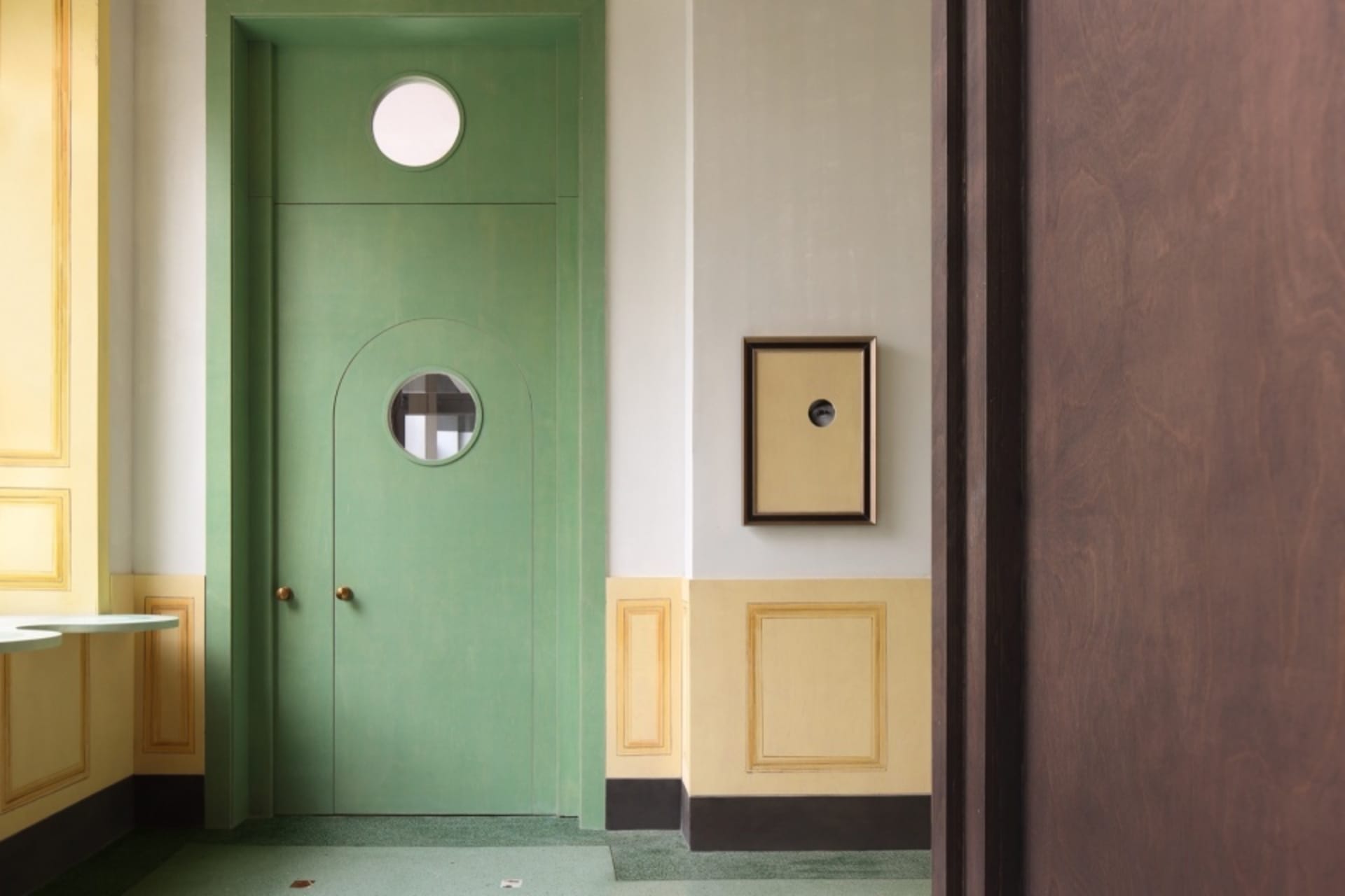 Empty green hallway with yellow trim and two doors, one with a round window