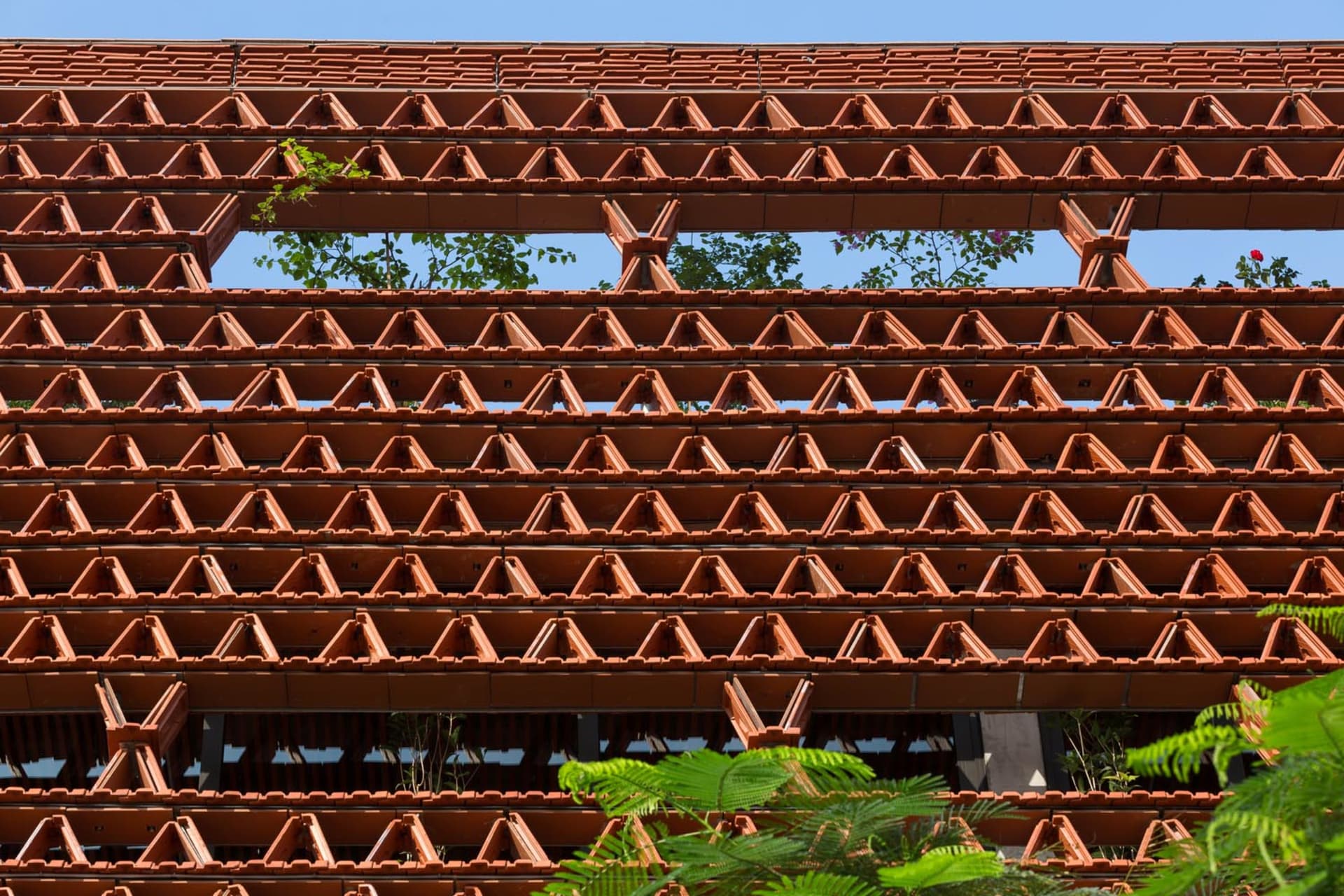 A brick building with many windows, surrounded by potted plants, conveying a sense of urban architecture and design