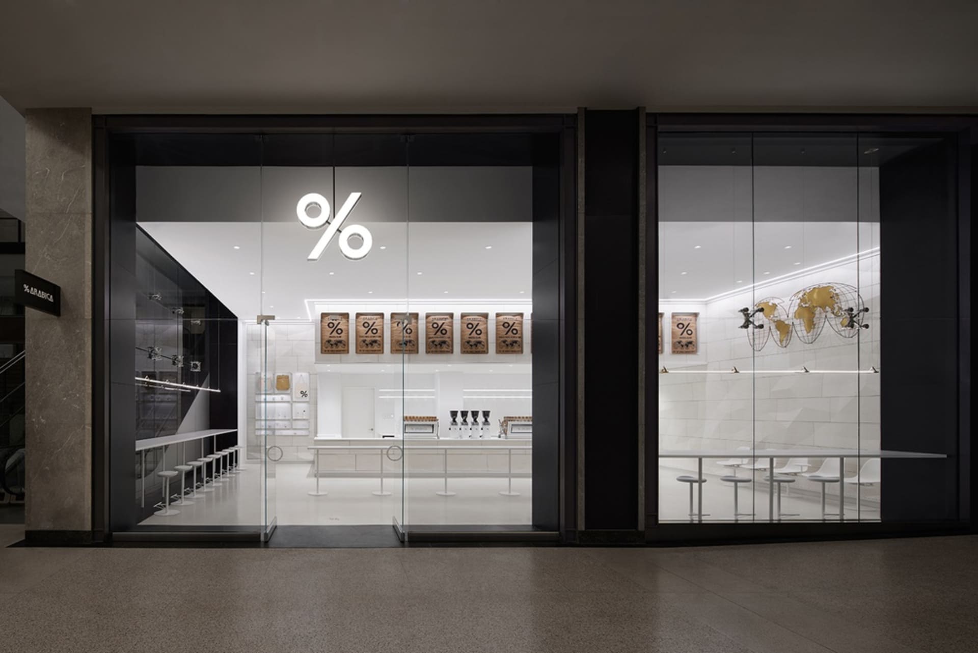 A modern cafe with a black and white theme, featuring a large glass window, tables, chairs, and bottles on display, creating an inviting and comfortable atmosphere