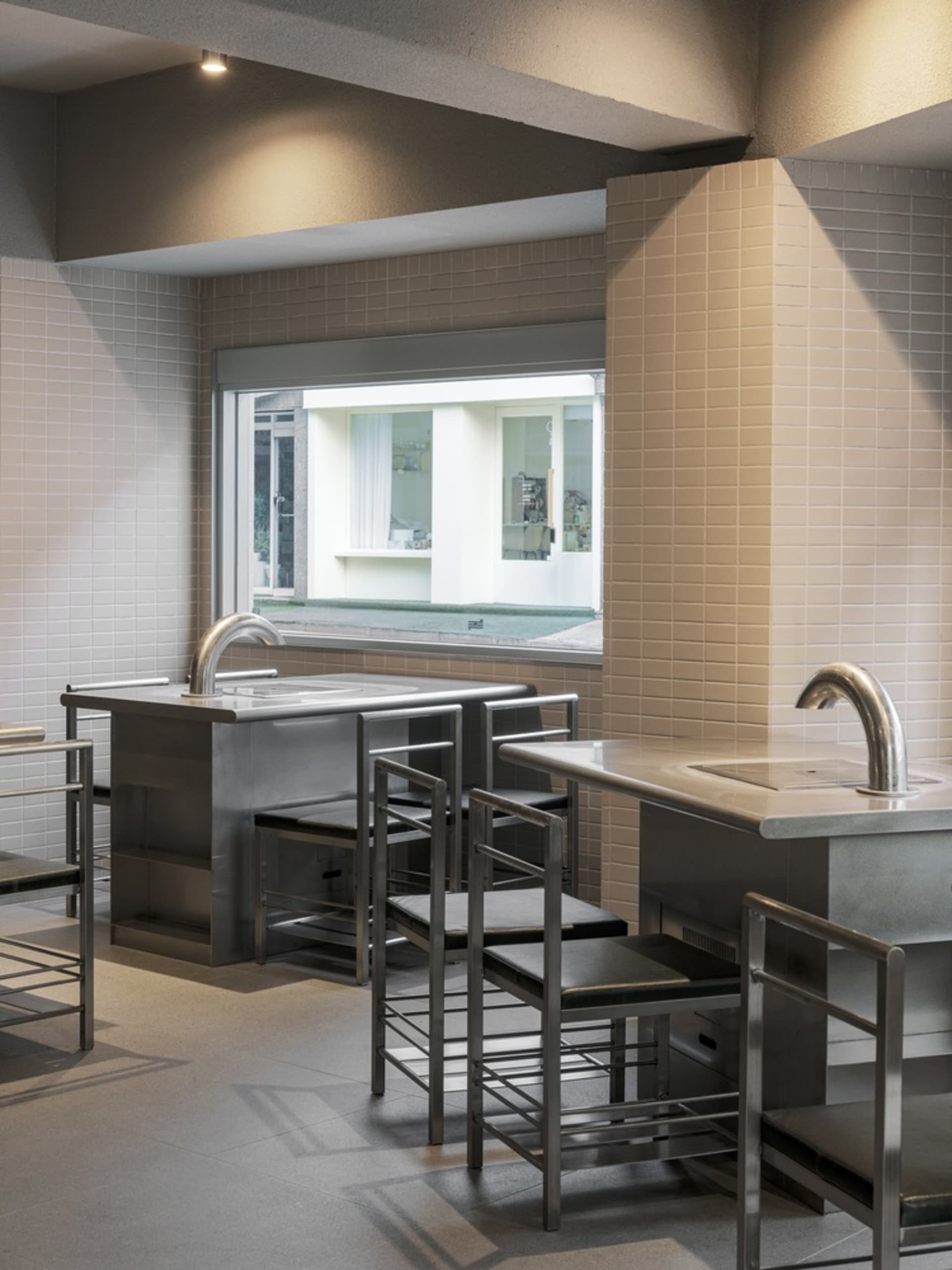 Empty kitchen with stainless steel appliances and fixtures, two sinks, and three chairs in a clean and well-organized space