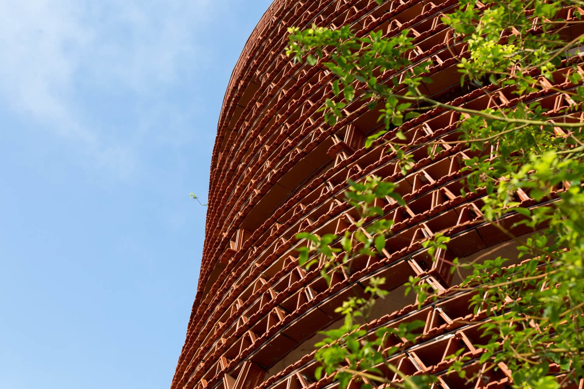 A modern building with a red brick exterior, multiple windows, and a natural setting with trees nearby
