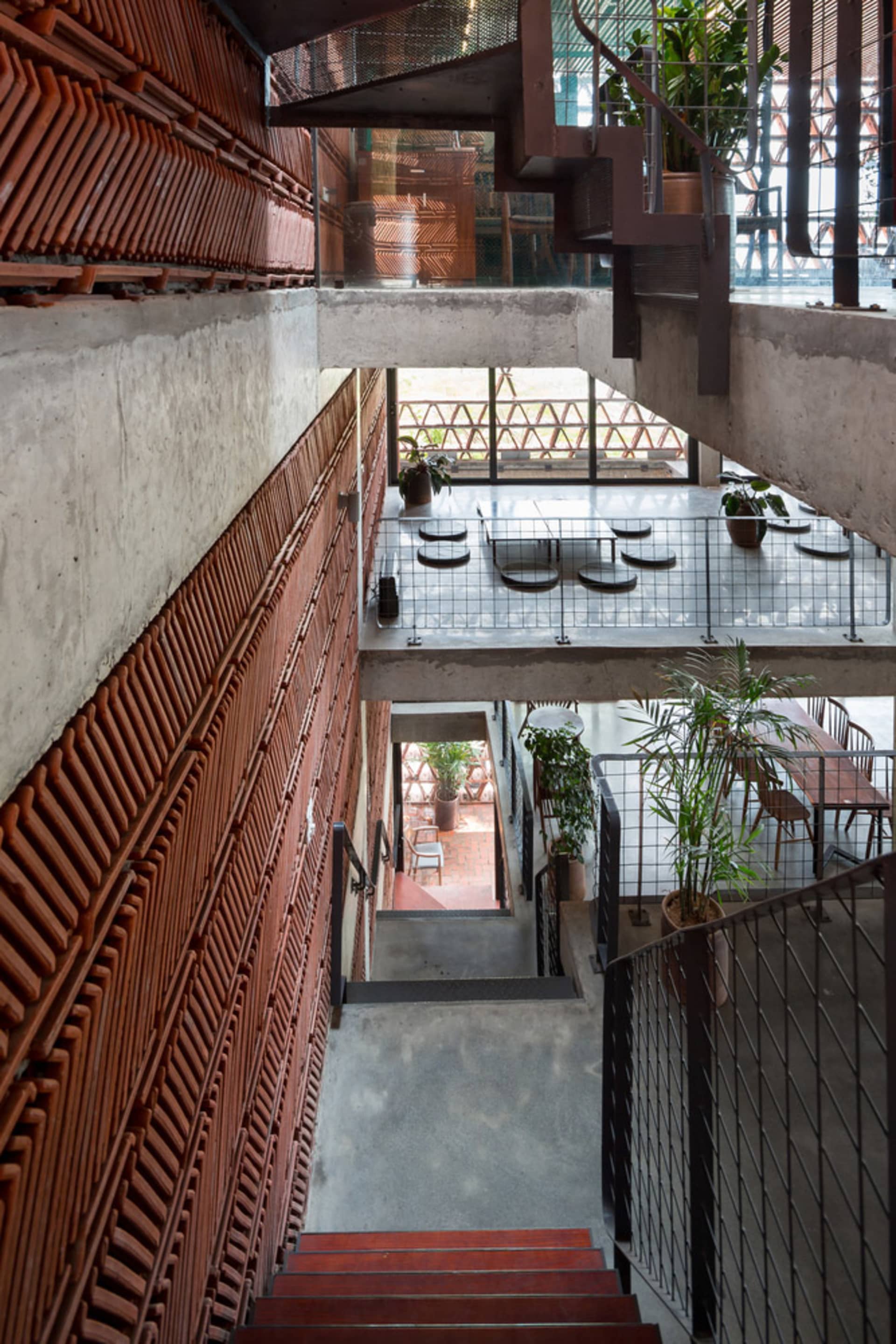 A modern stairwell with concrete stairs, well-lit and decorated with potted plants and chairs, creating a comfortable seating area