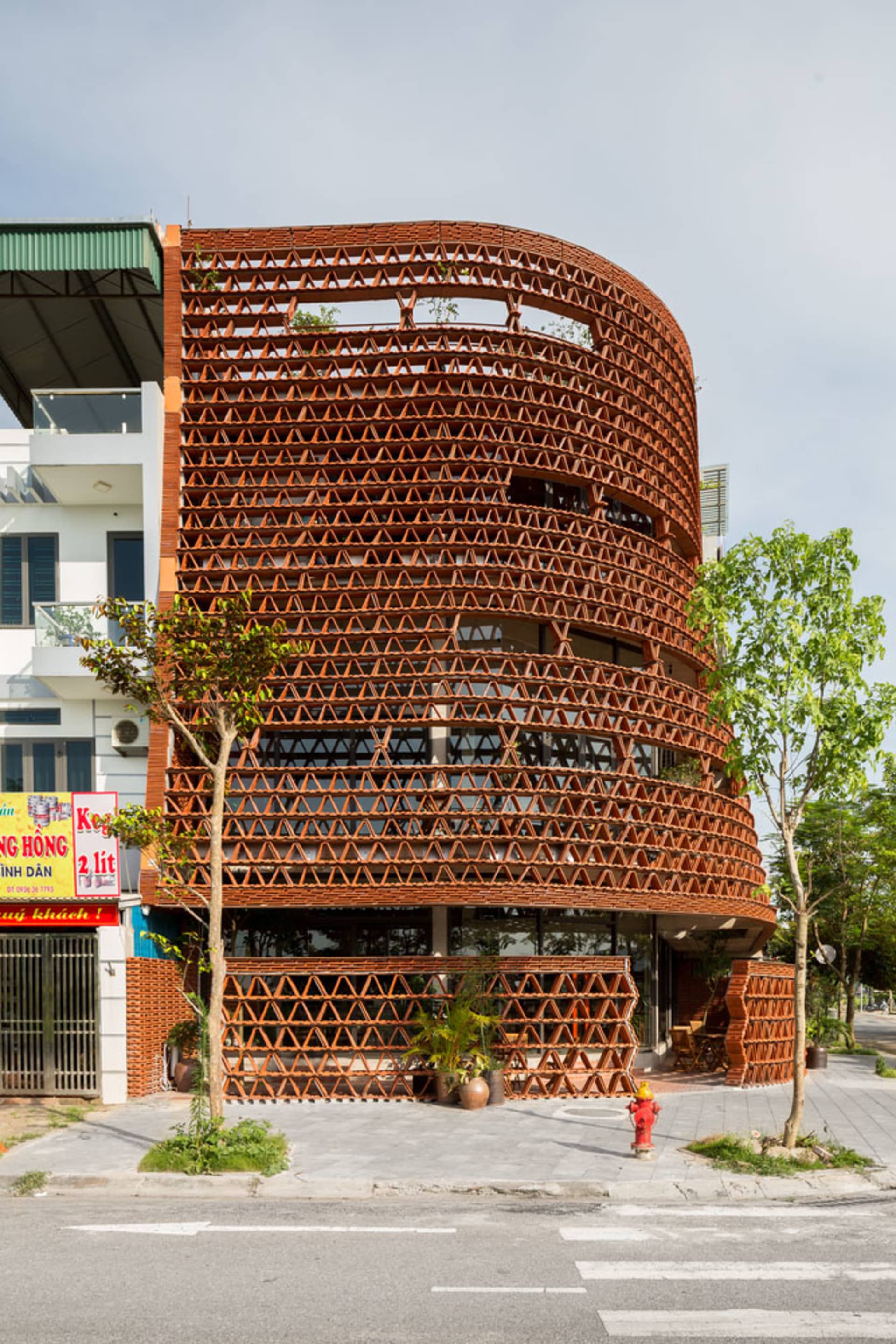 A public space with a brick exterior, brown color scheme, and several windows, featuring potted plants and two chairs