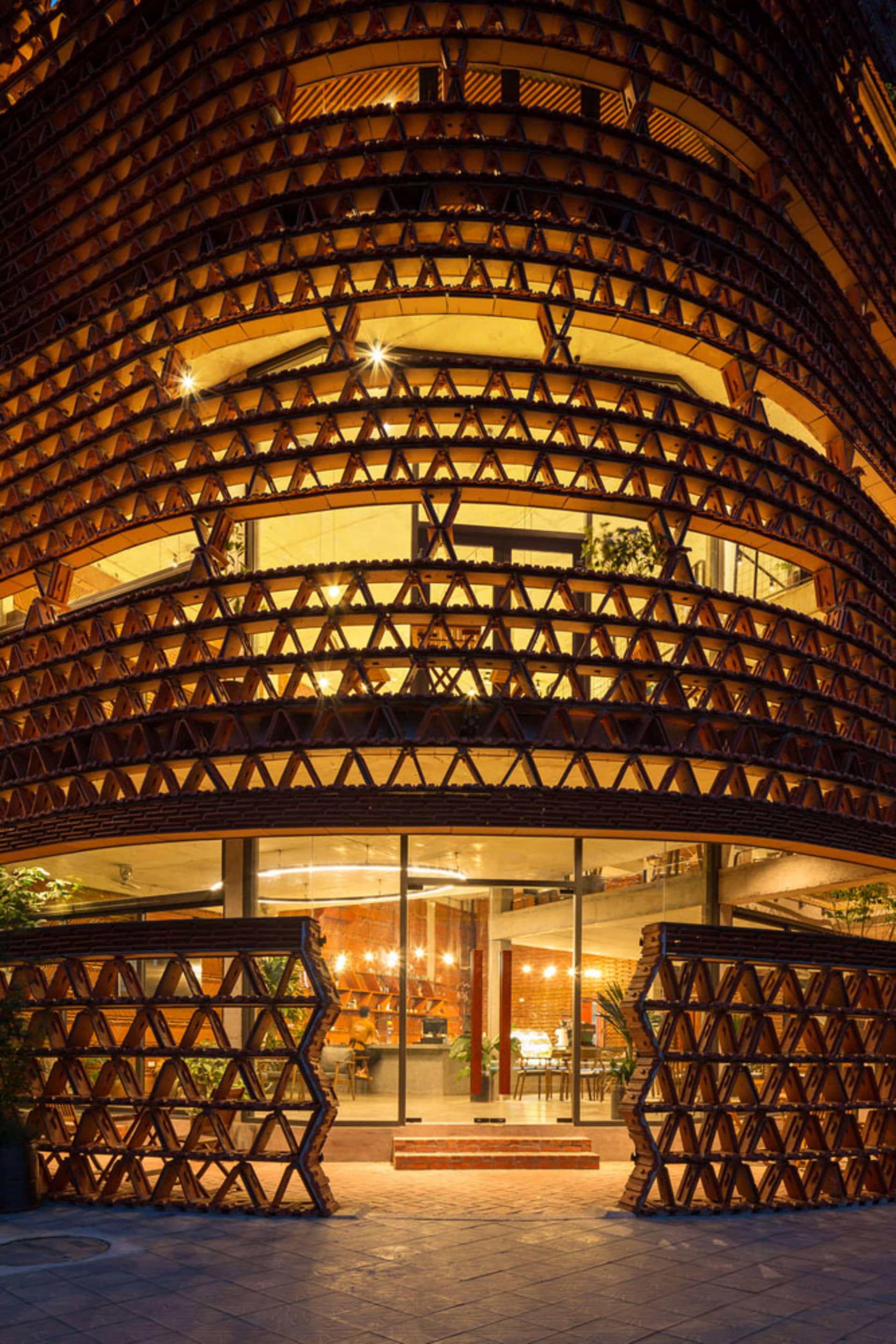 A modern building with a large wooden structure in front, featuring a seating area with chairs and potted plants both inside and outside