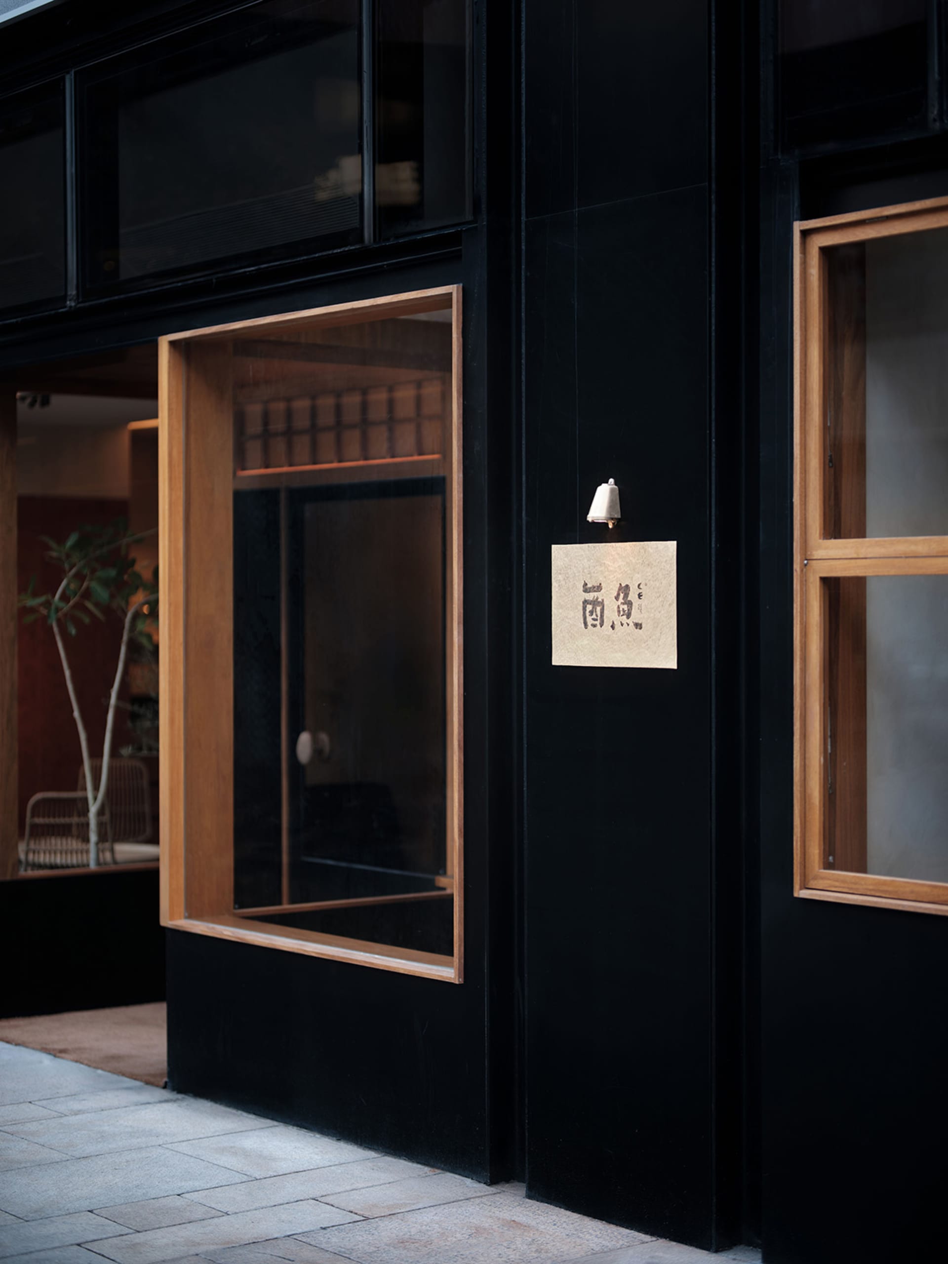 A storefront with a black door and window, surrounded by potted plants and a signboard written in Chinese characters in a cultural and commercial setting