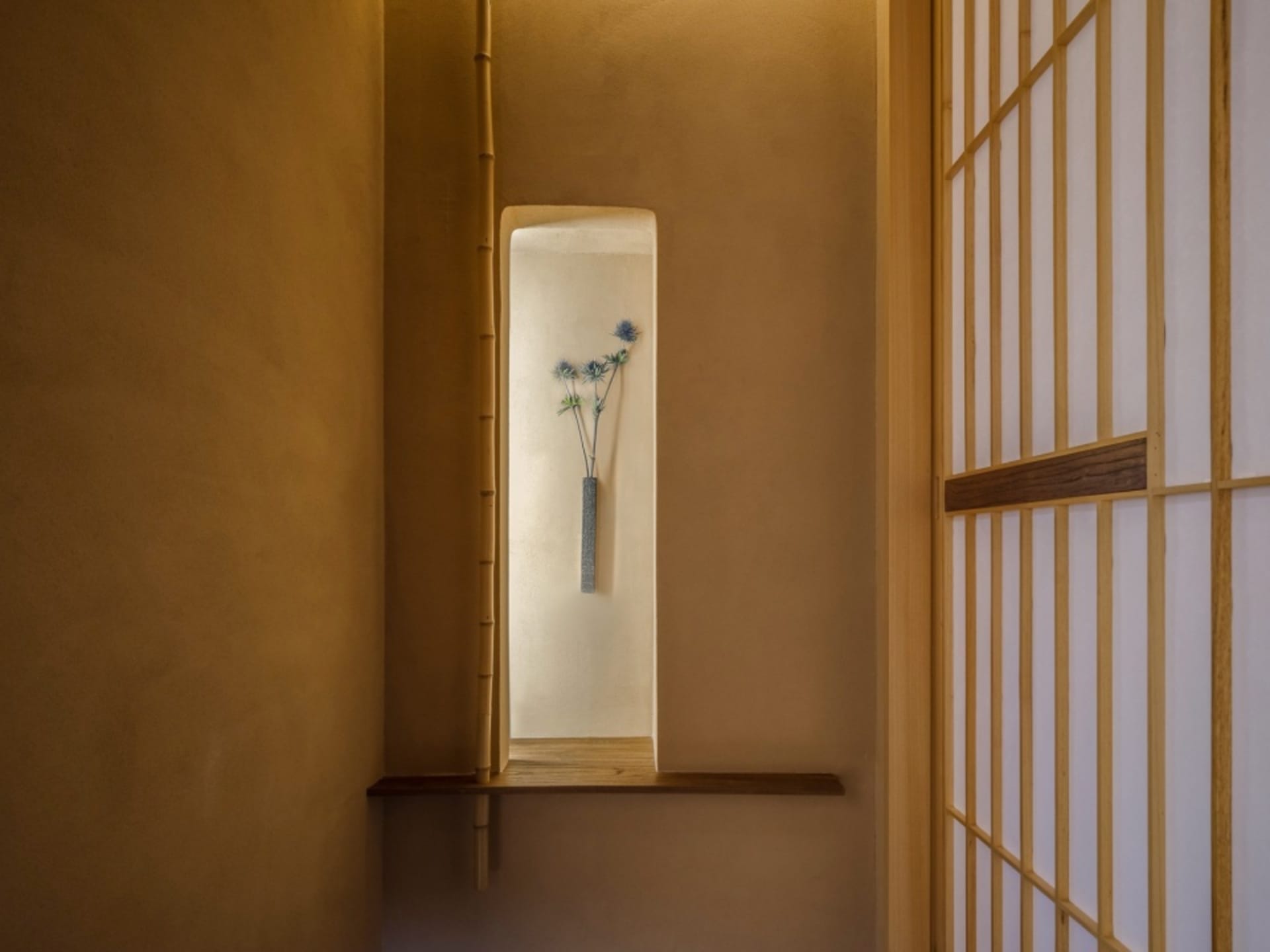 A calm and serene hallway with a concrete wall, two vases with flowers, and a minimalist aesthetic
