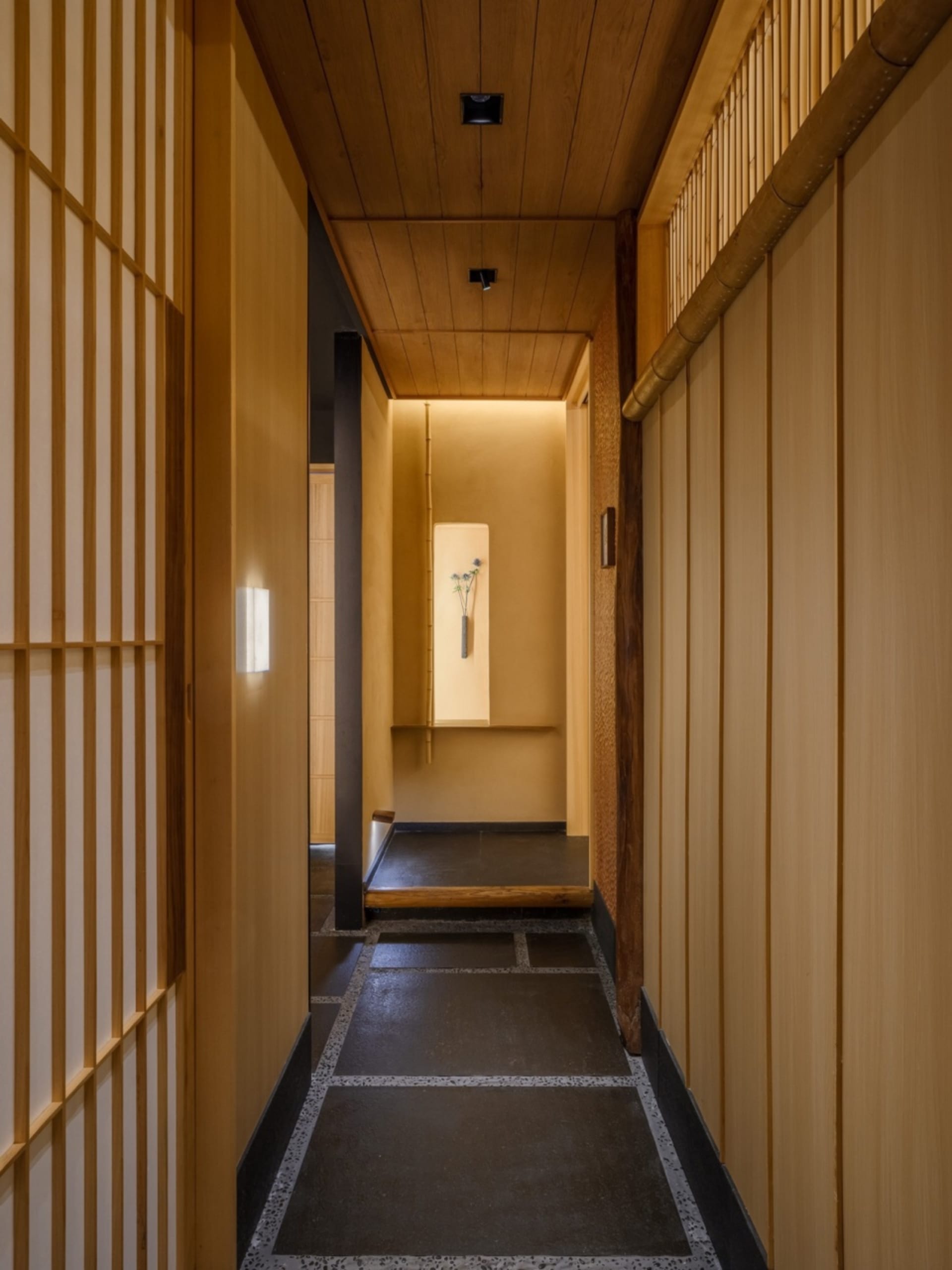 Narrow hallway with wooden walls and floors, featuring two doors and a dark atmosphere due to lack of natural light