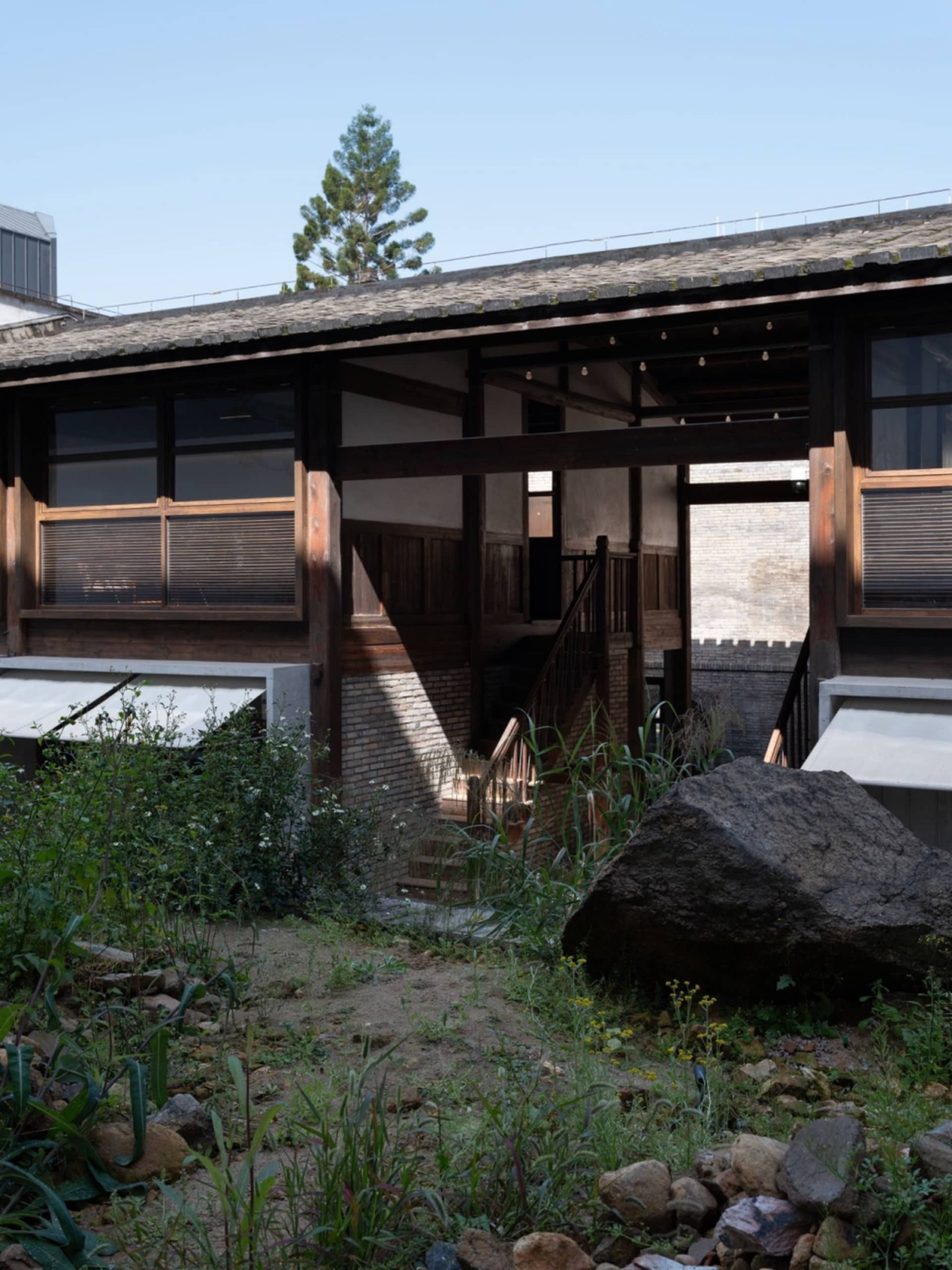 A traditional Asian building with a rock wall and wooden structure, featuring a courtyard area with a stone wall and a large rock, and windows on the side