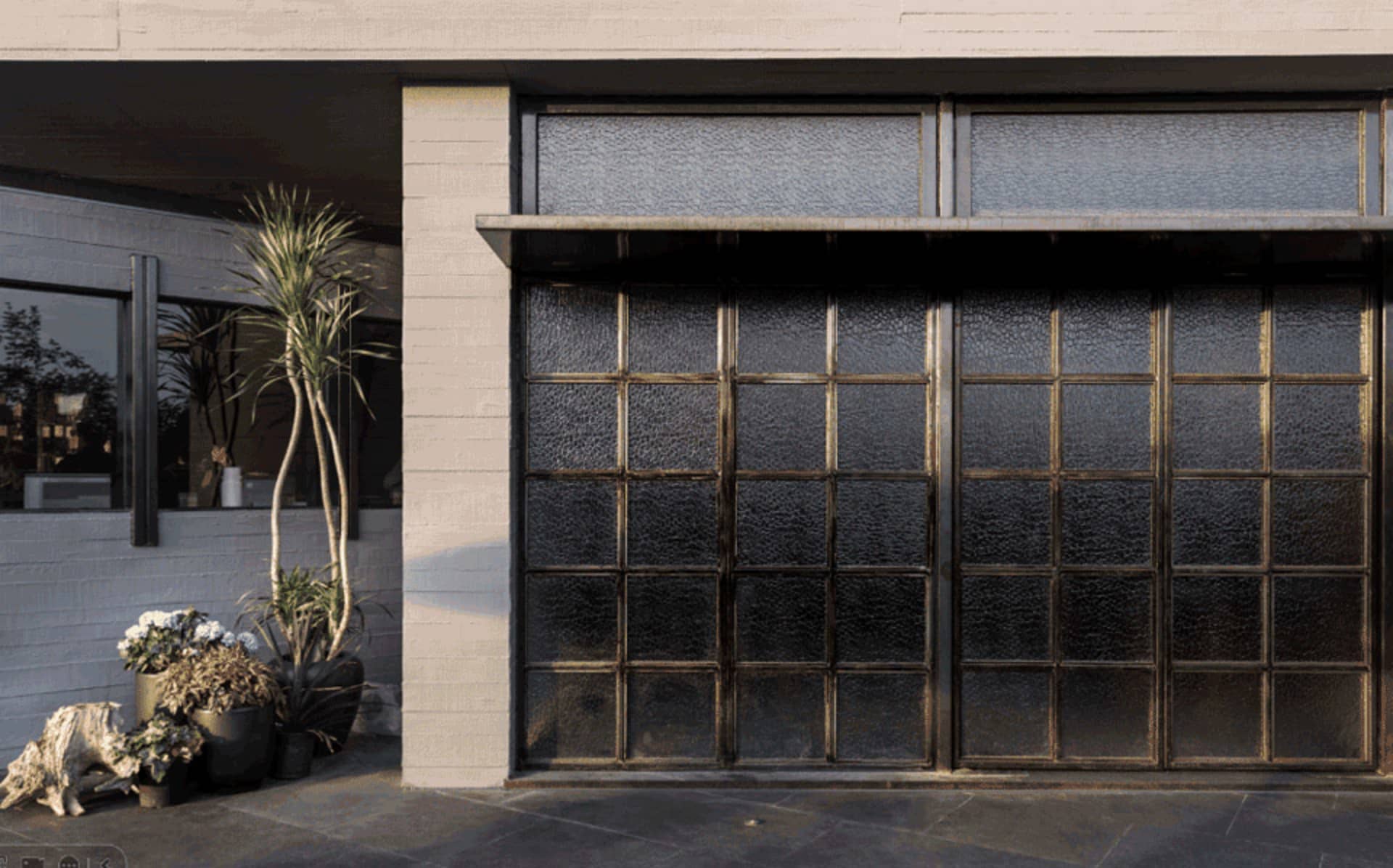 A modern house entrance with two large glass doors, a metal frame, and a potted plant on the left side
