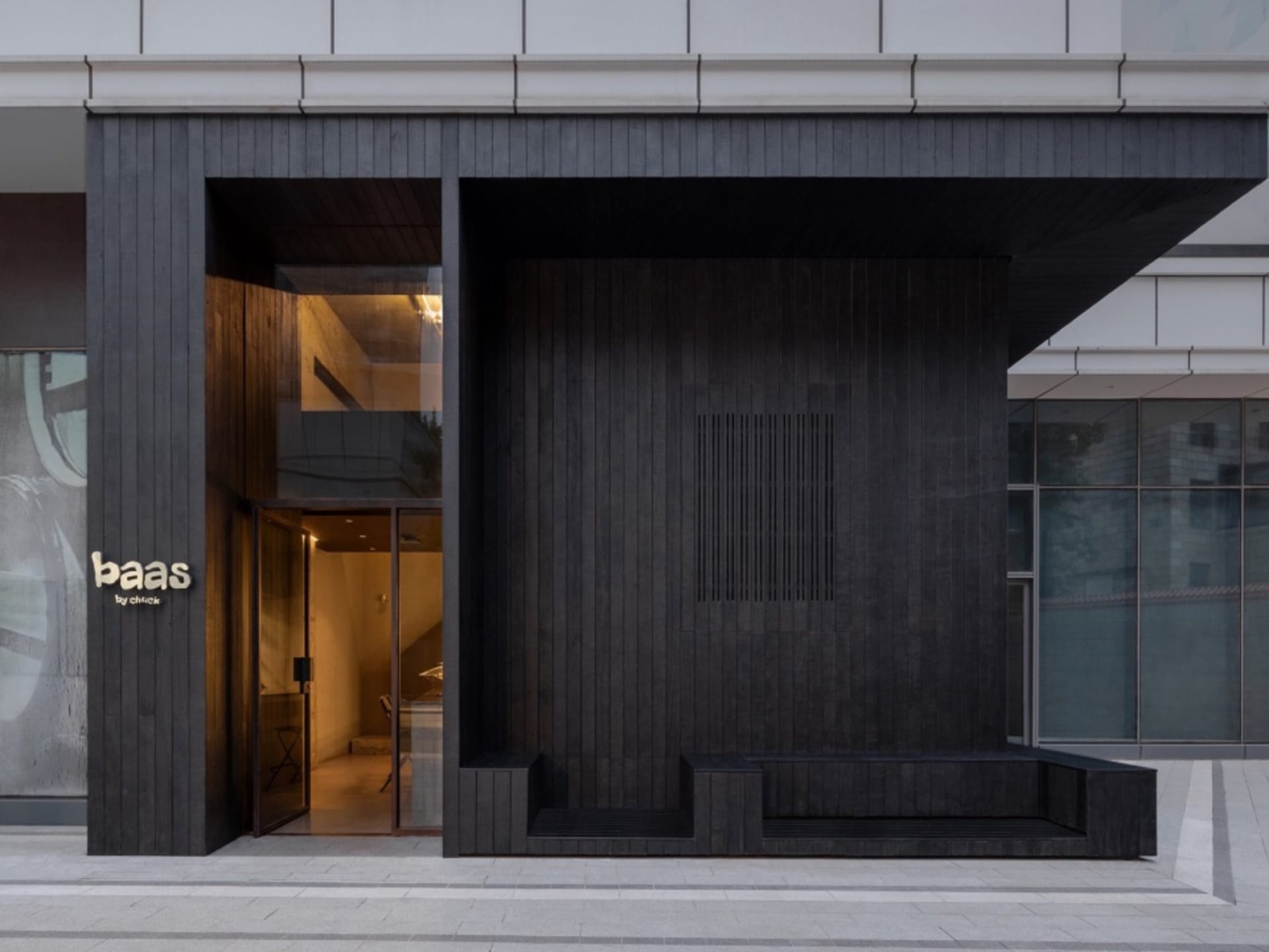 Modern building exterior with a black wooden structure, large window, and minimalist benches in front