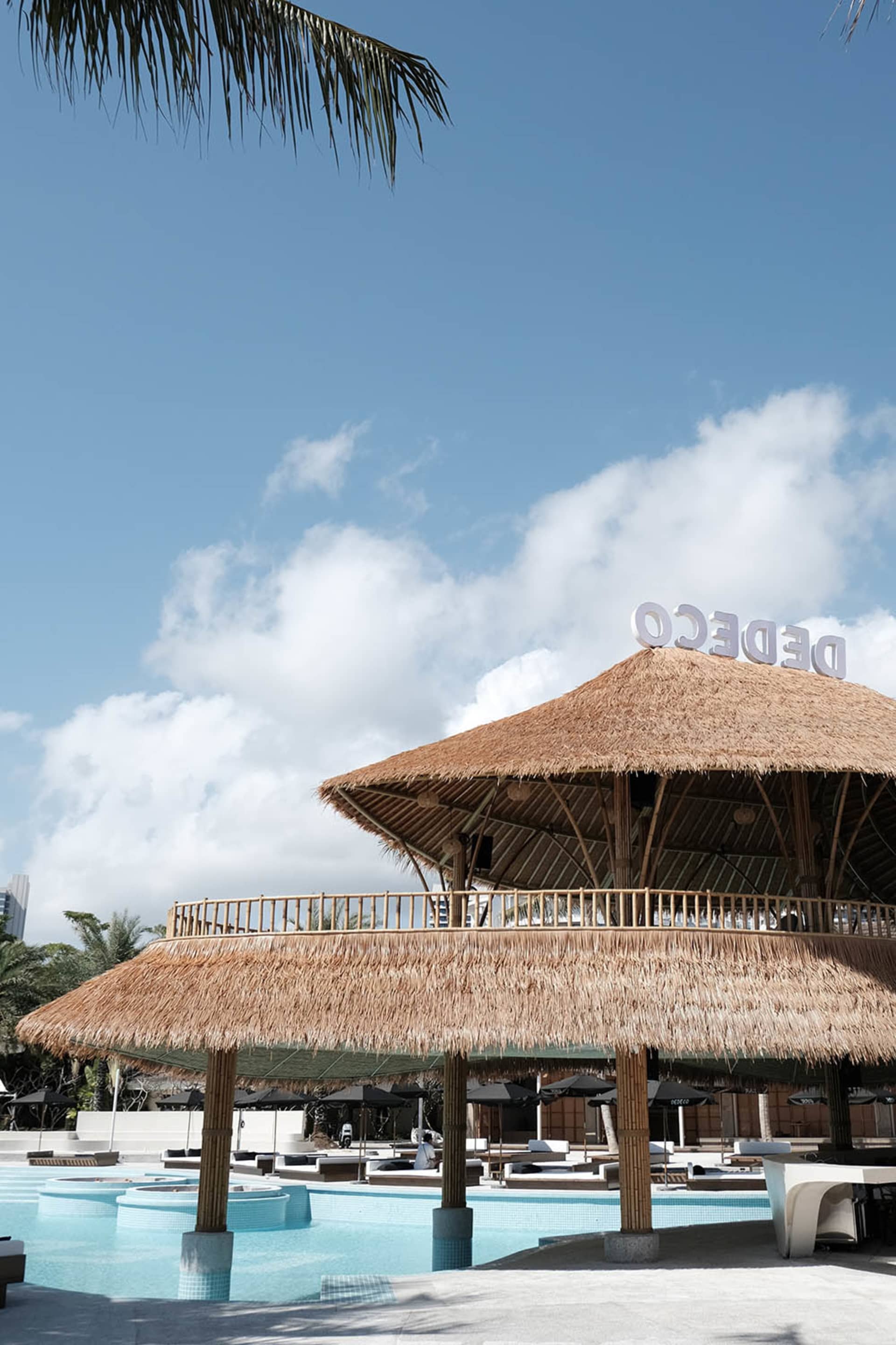 Open-air restaurant with a thatched roof, surrounded by chairs and tables, in a tropical atmosphere