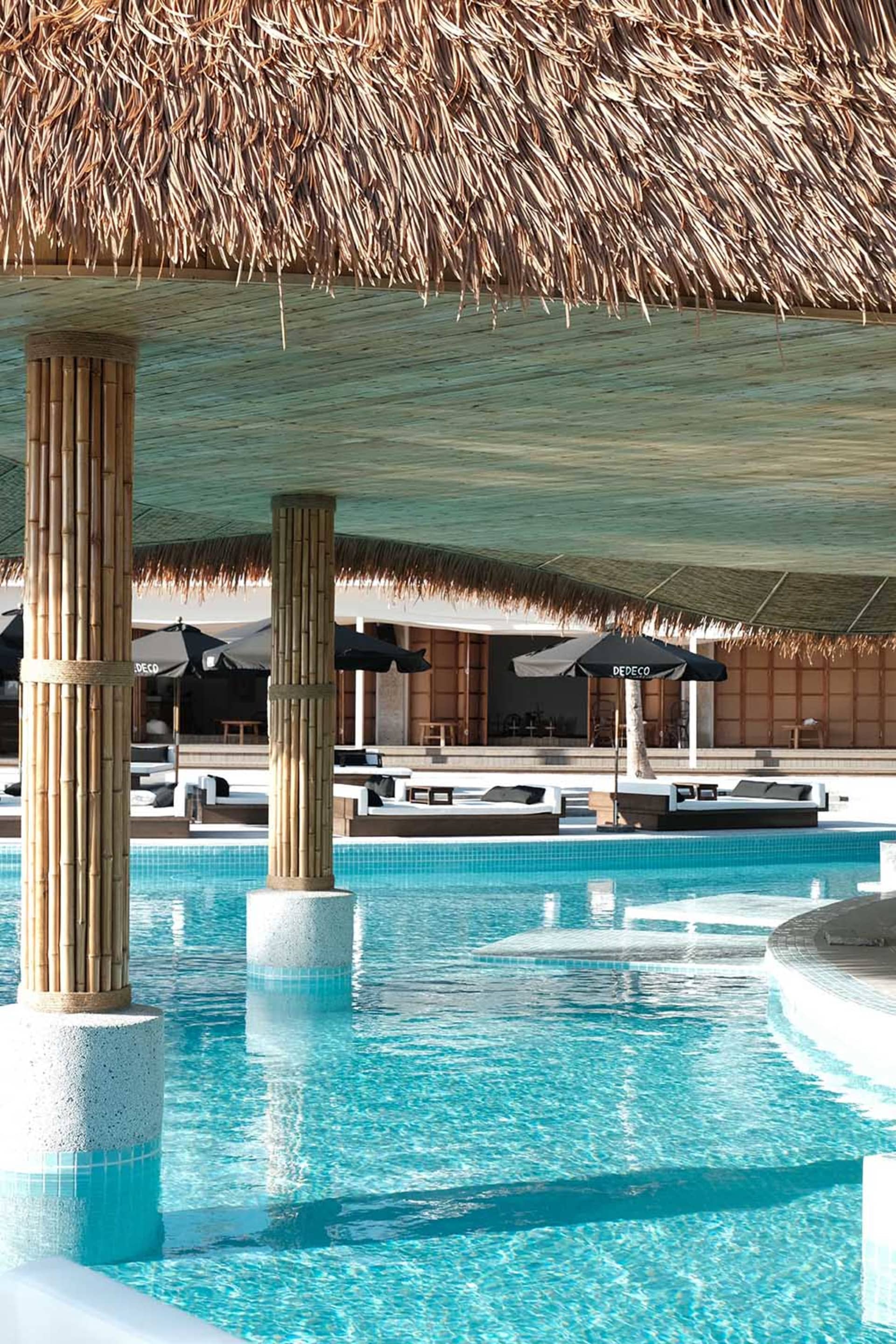 A pool area with a large pool surrounded by chairs and umbrellas, providing a comfortable outdoor space for relaxation