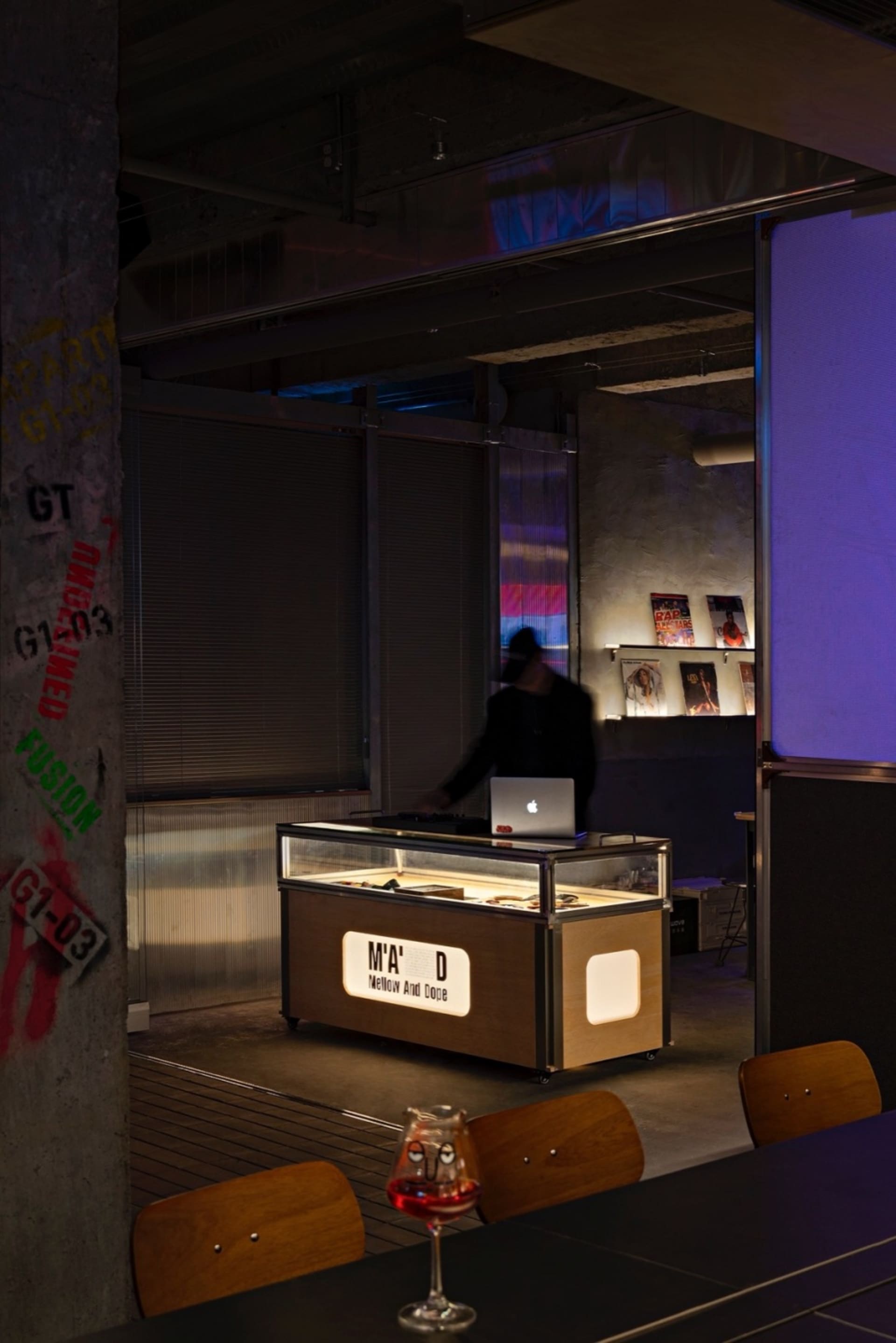 Office space with a wooden table, glass display case, and modern furniture, featuring a desk with a laptop and two people