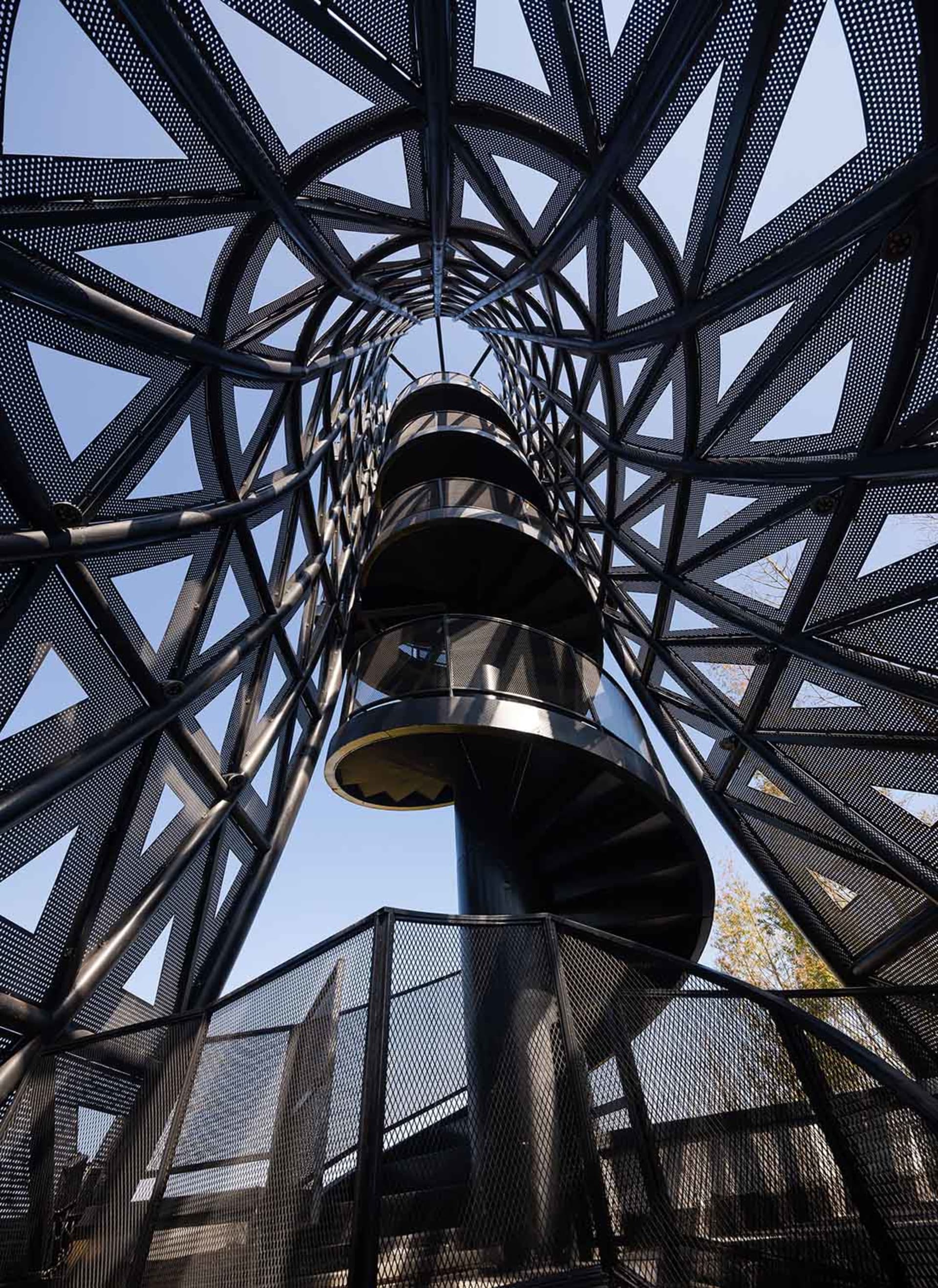 A rendered image of a spiral staircase with a black metal railing and surrounding structure, set against a blank background