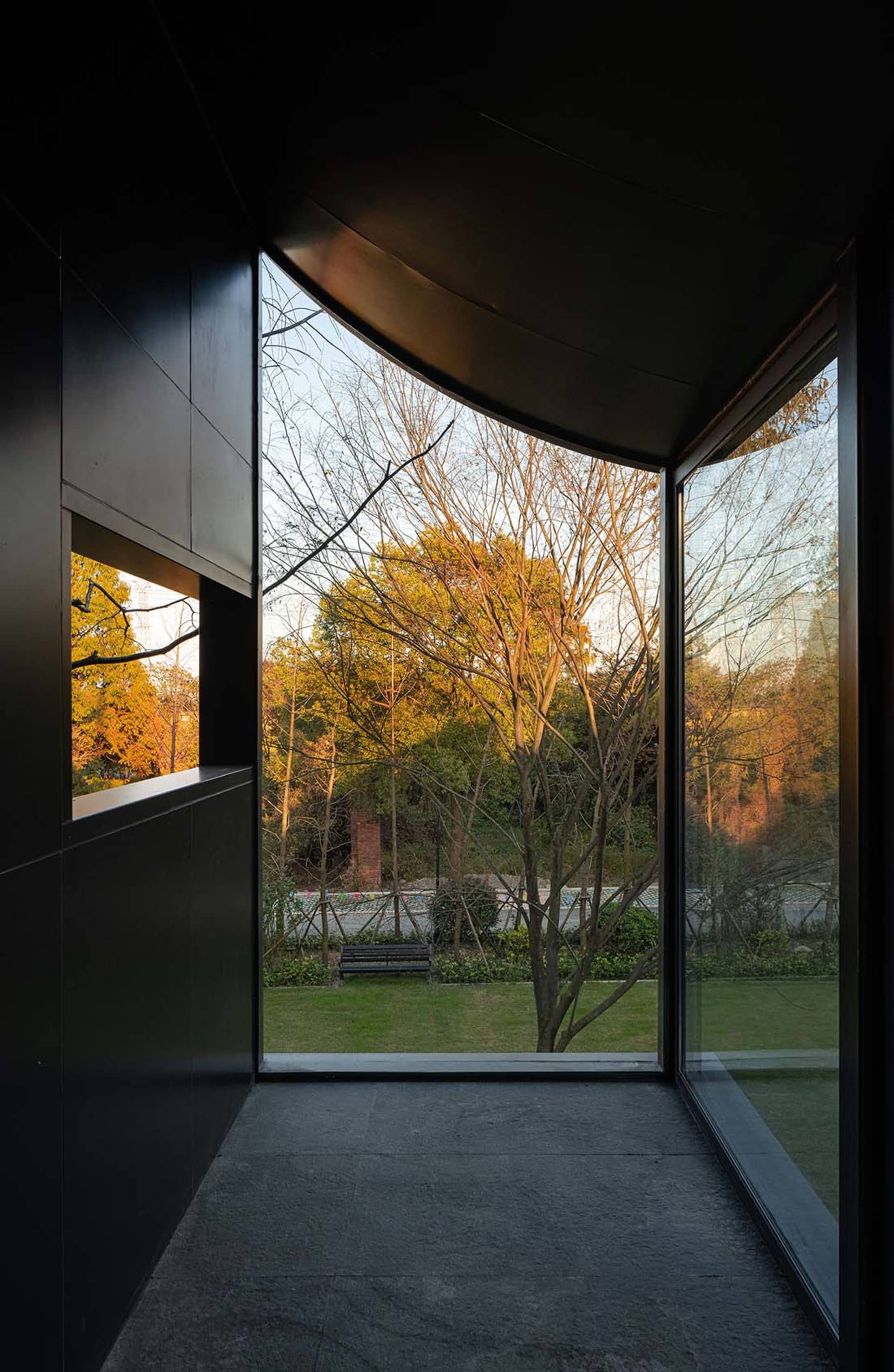 A calm office space with a black building facade, wooden benches, and a large window offering a view of trees outside
