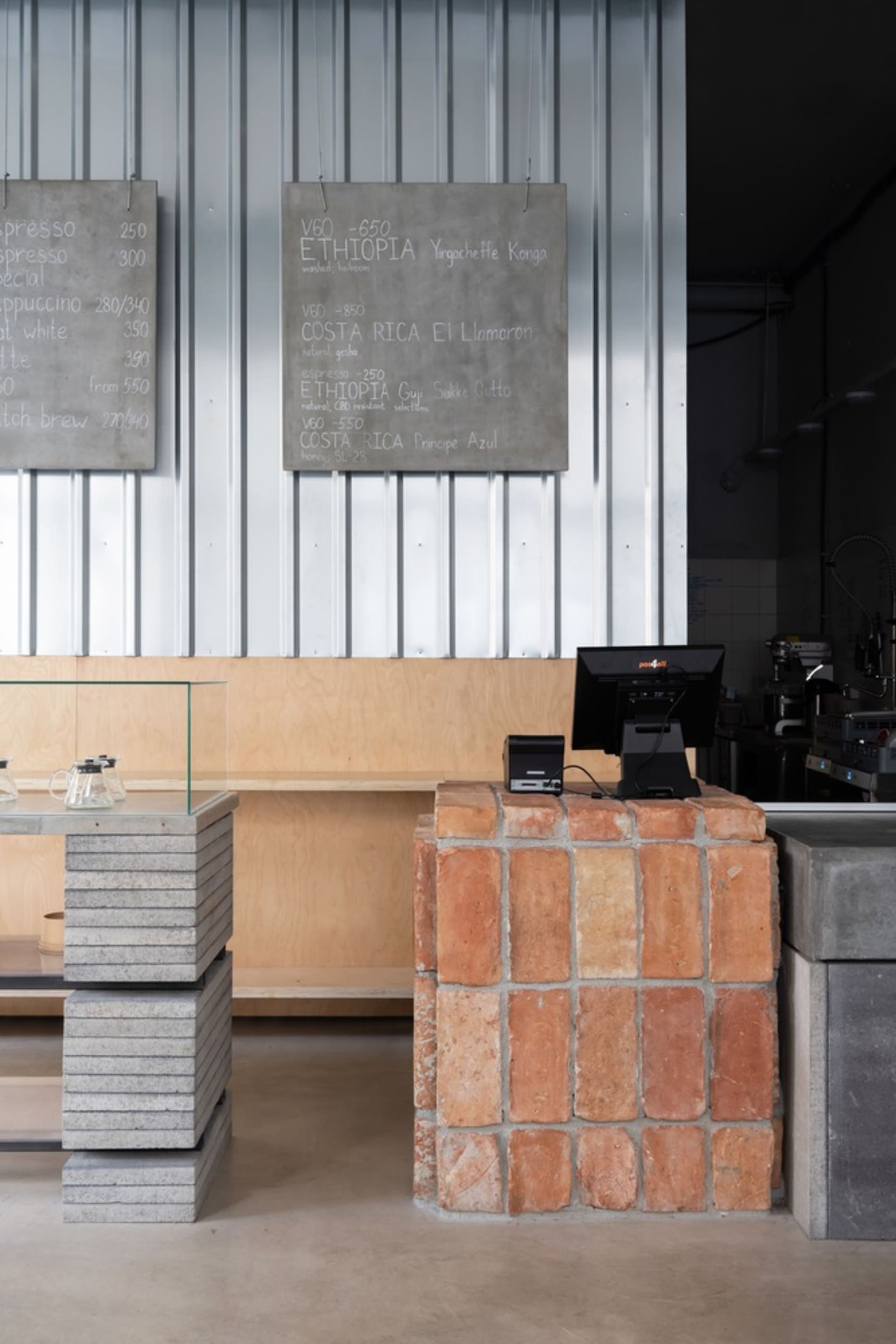 Casual restaurant interior with a brick wall, wooden counter, and dining table, featuring cups, bowls, bottles, and books