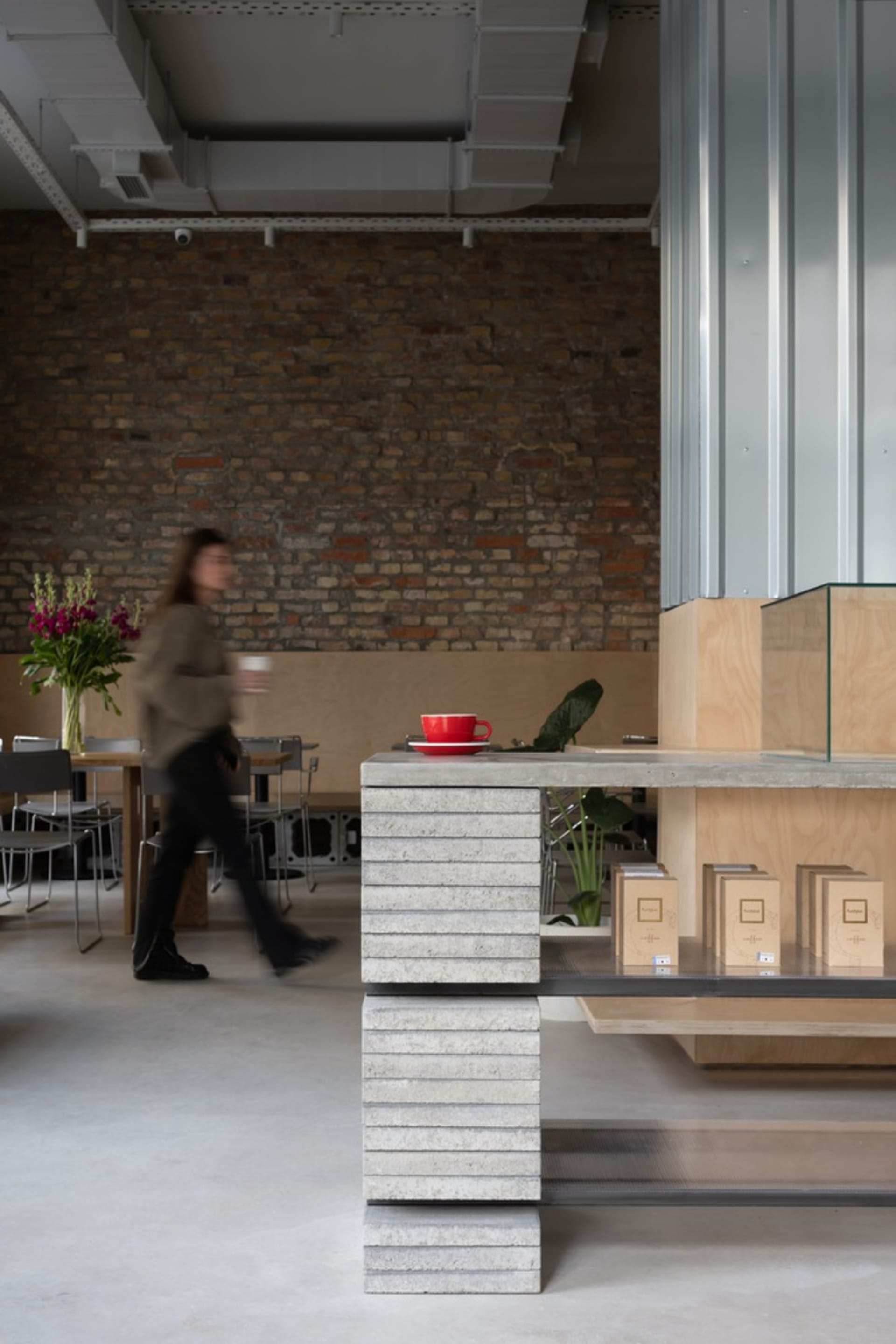 A rustic cafe interior with a brick wall, potted plants, and a counter with displayed items and cups