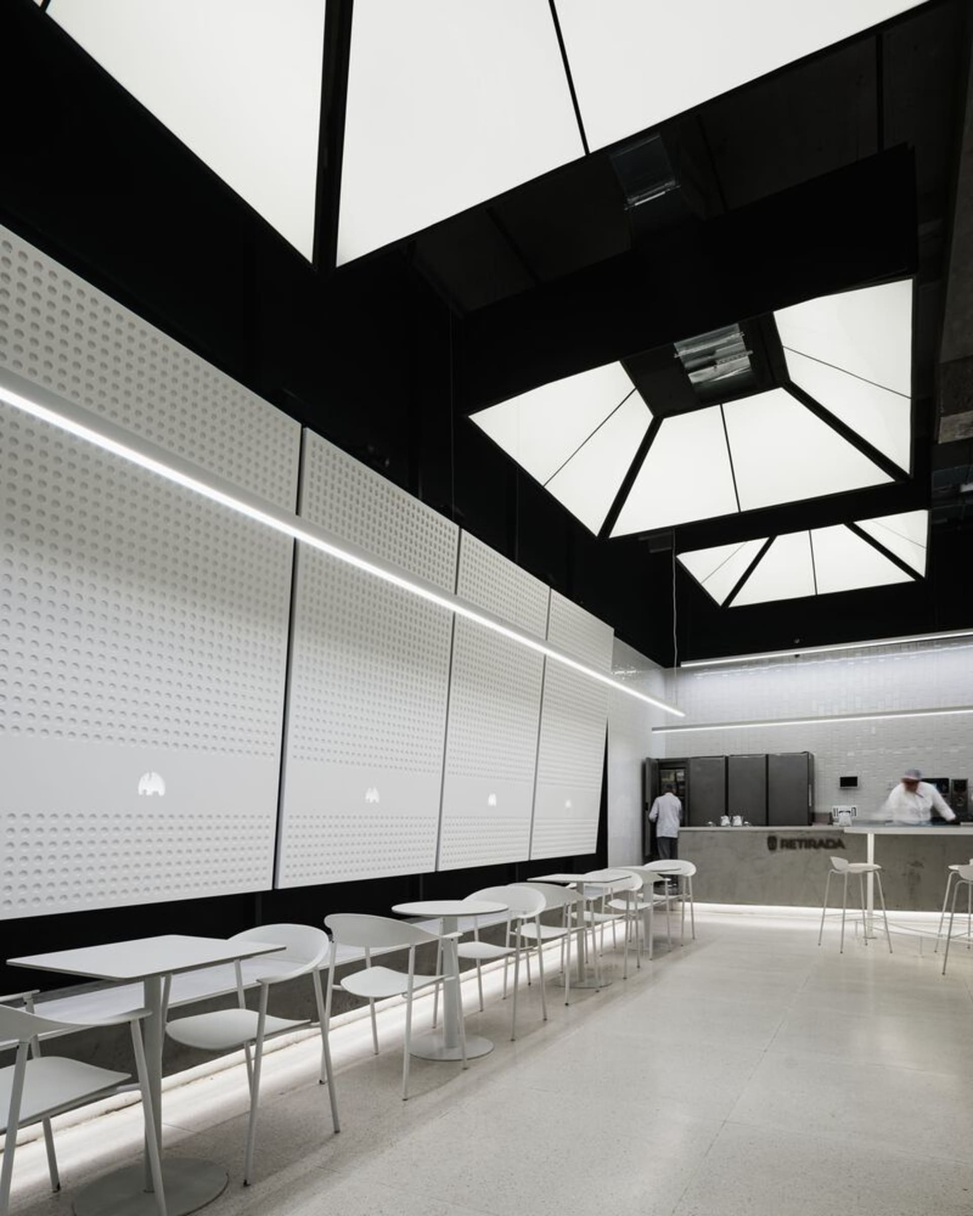 空蕩蕩的餐廳內部，白色牆面、餐桌與舒適座椅安排，展現現代簡約風格與精心規劃的燈光