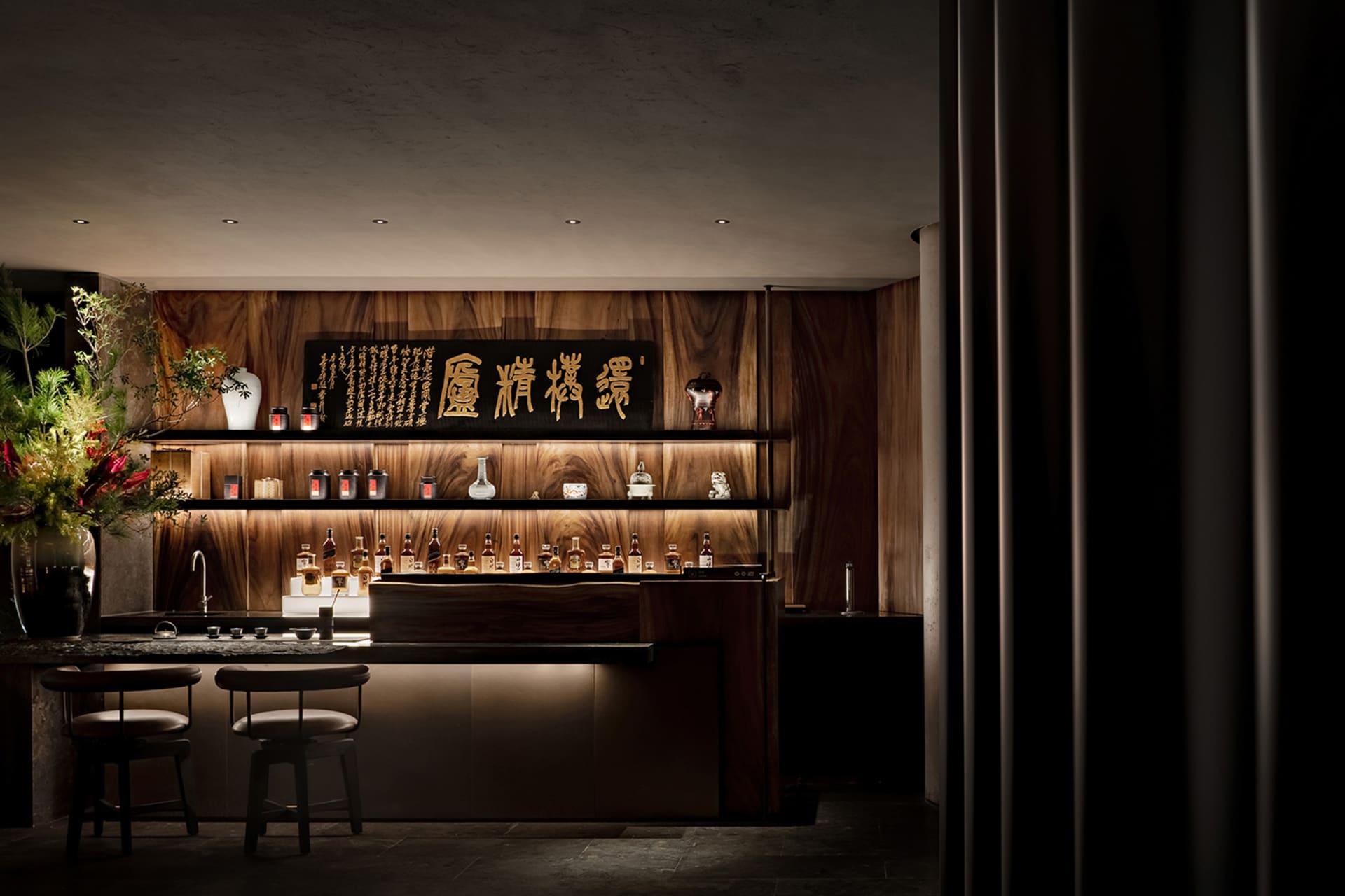 Warm and inviting Asian restaurant with wooden walls, a bar area featuring bottles of liquor, wine glasses, and decorative vases