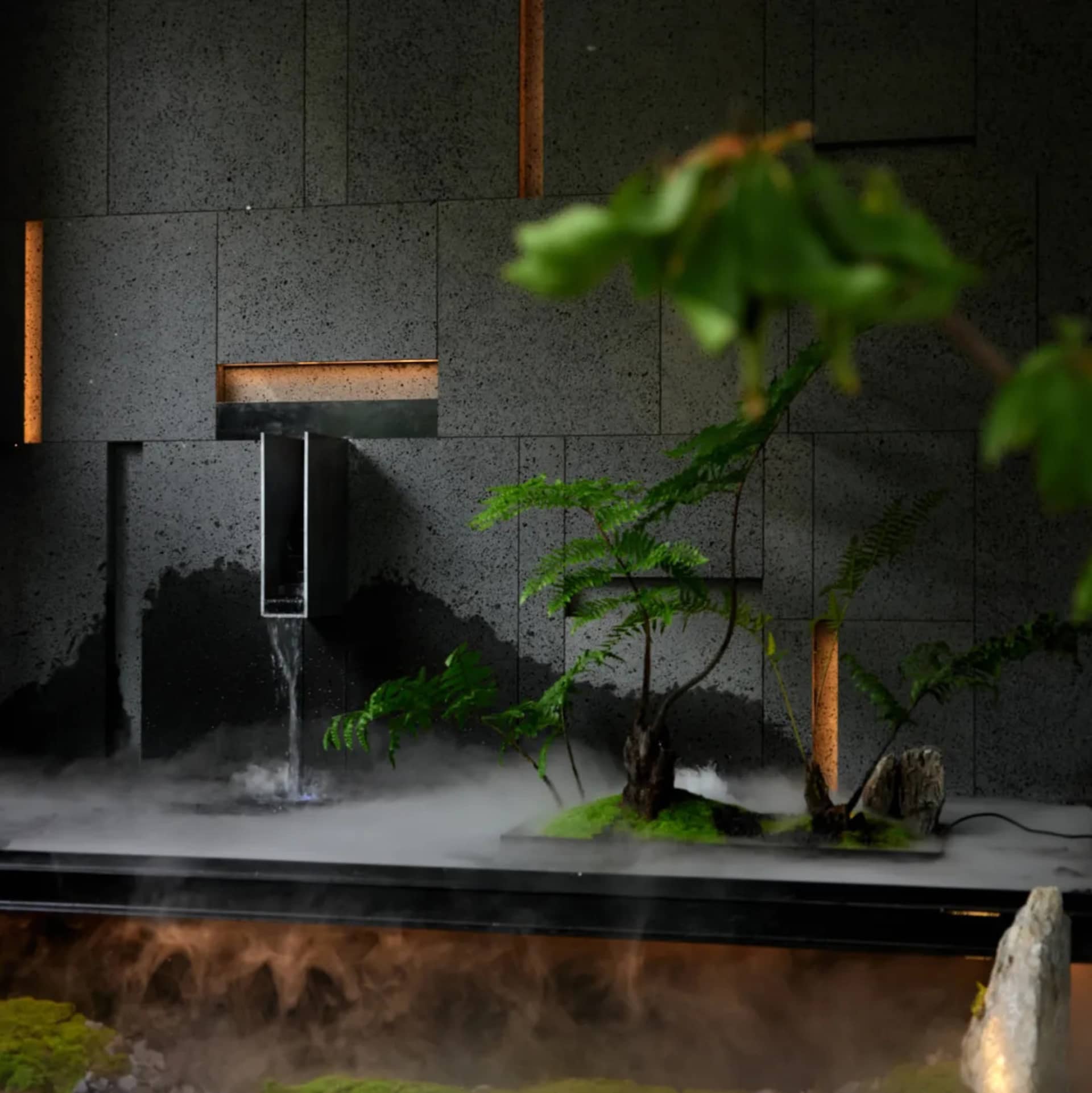 A serene indoor space with a large stone wall, a central fountain, and potted plants on either side