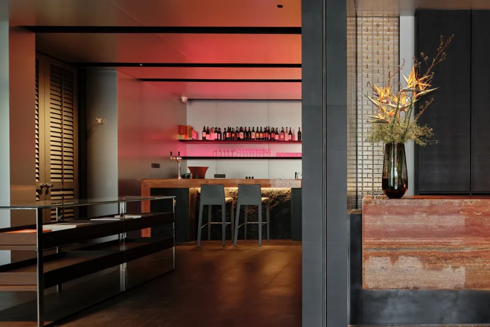 Elegant bar area with a counter, two chairs, and a vase on display, surrounded by bottles, creating a comfortable environment for patrons to enjoy their drinks and socialize