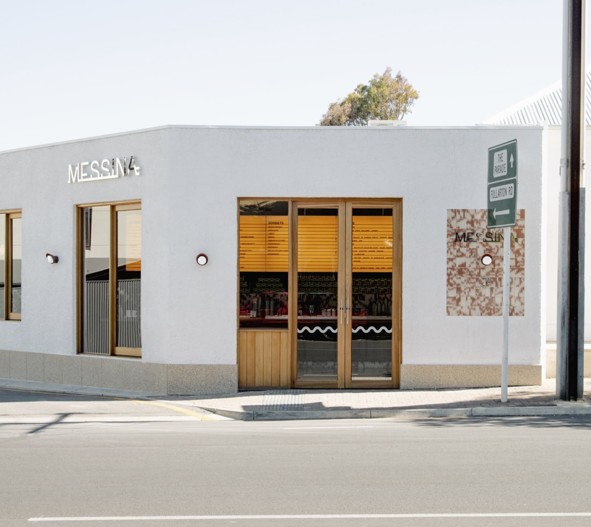 Exterior view of a small white building with a wooden door and bottles on the sidewalk