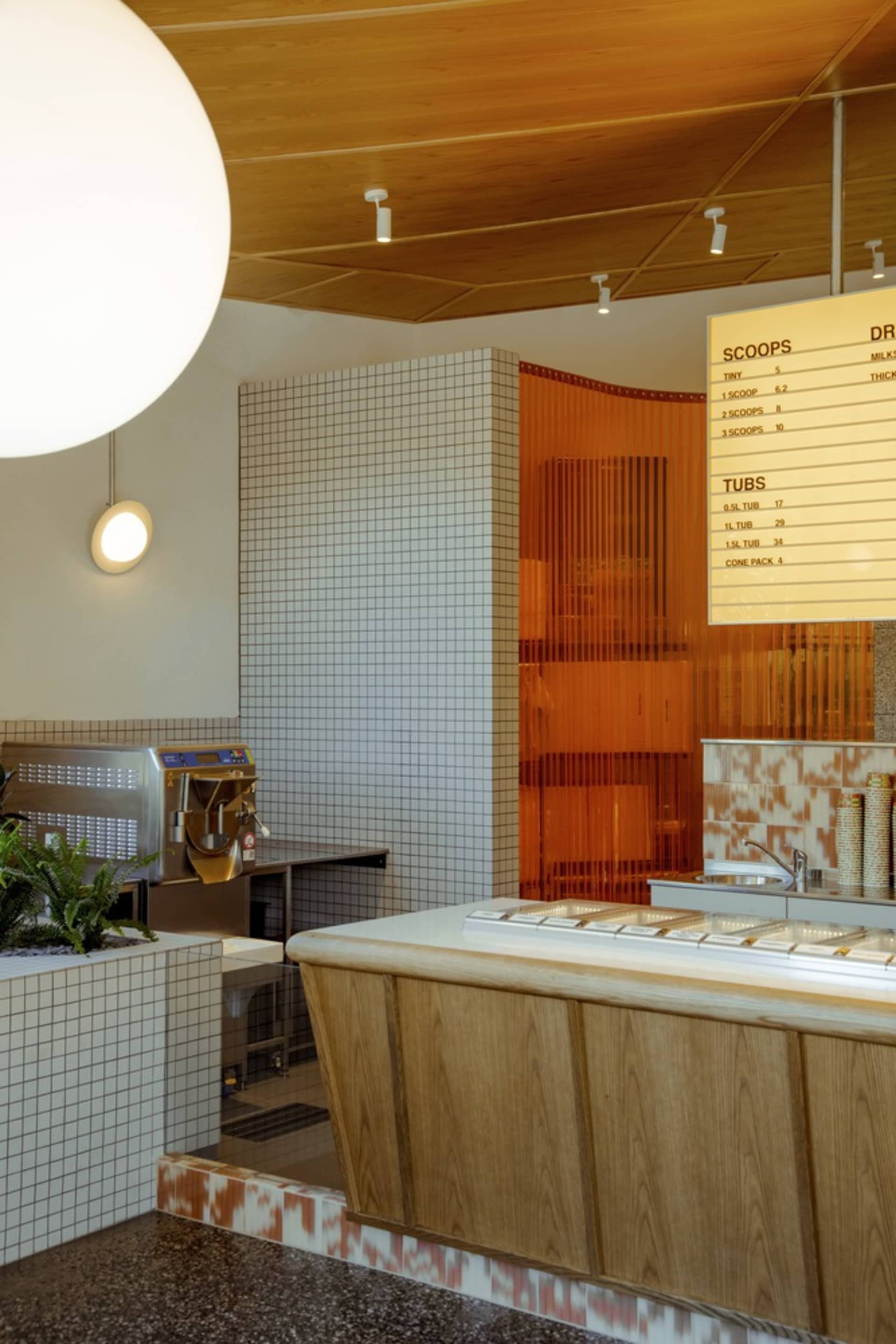 Modern restaurant kitchen with a counter featuring a drink machine and refrigerator, two sinks, and various items and potted plants