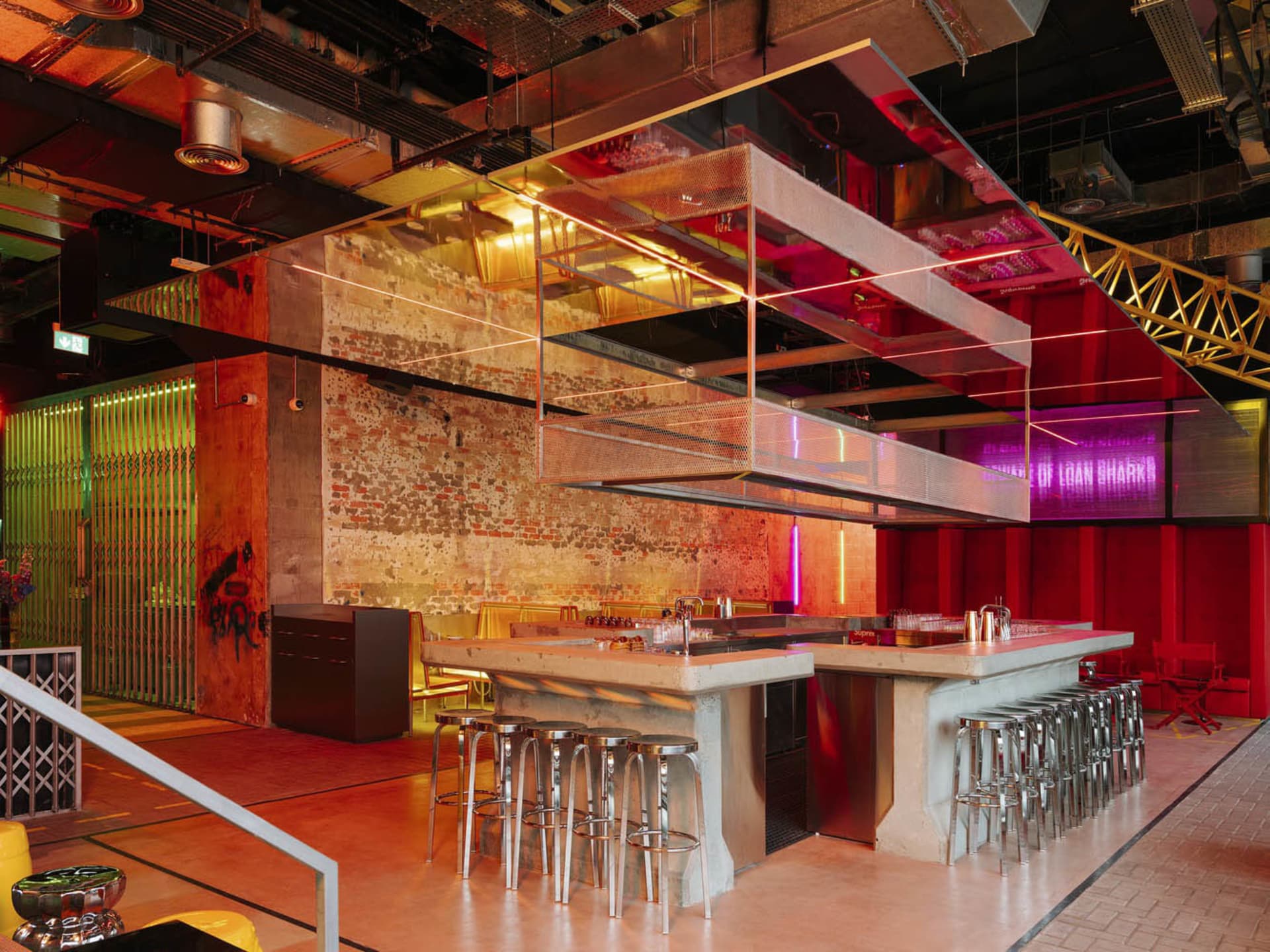 Industrial kitchen with a modern design, featuring a large island, stools, chairs, and a red-painted wall, with a warm atmosphere created by red lighting
