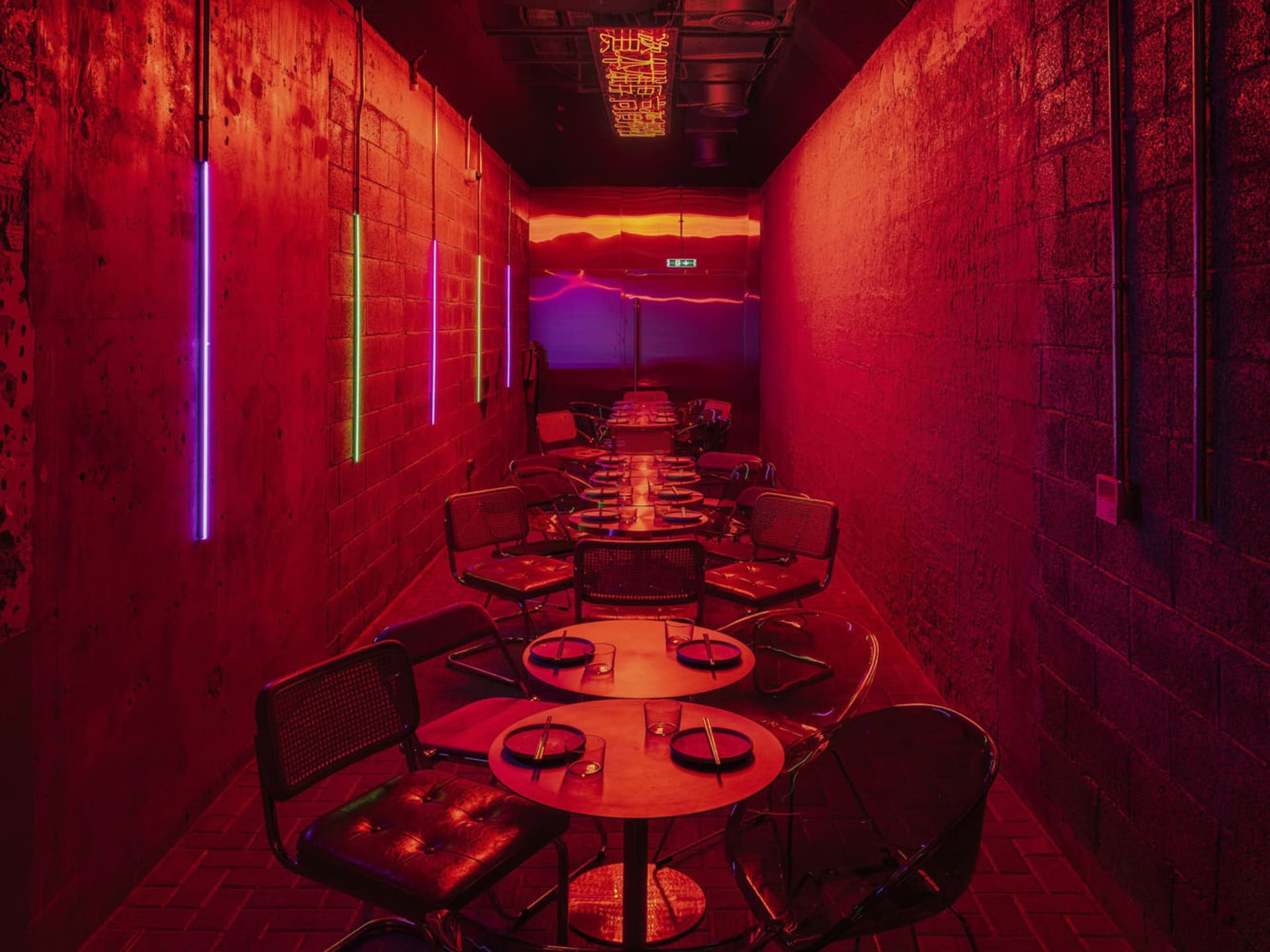 Dimly lit dining area with multiple tables and chairs, red brick walls, and a cozy ambiance