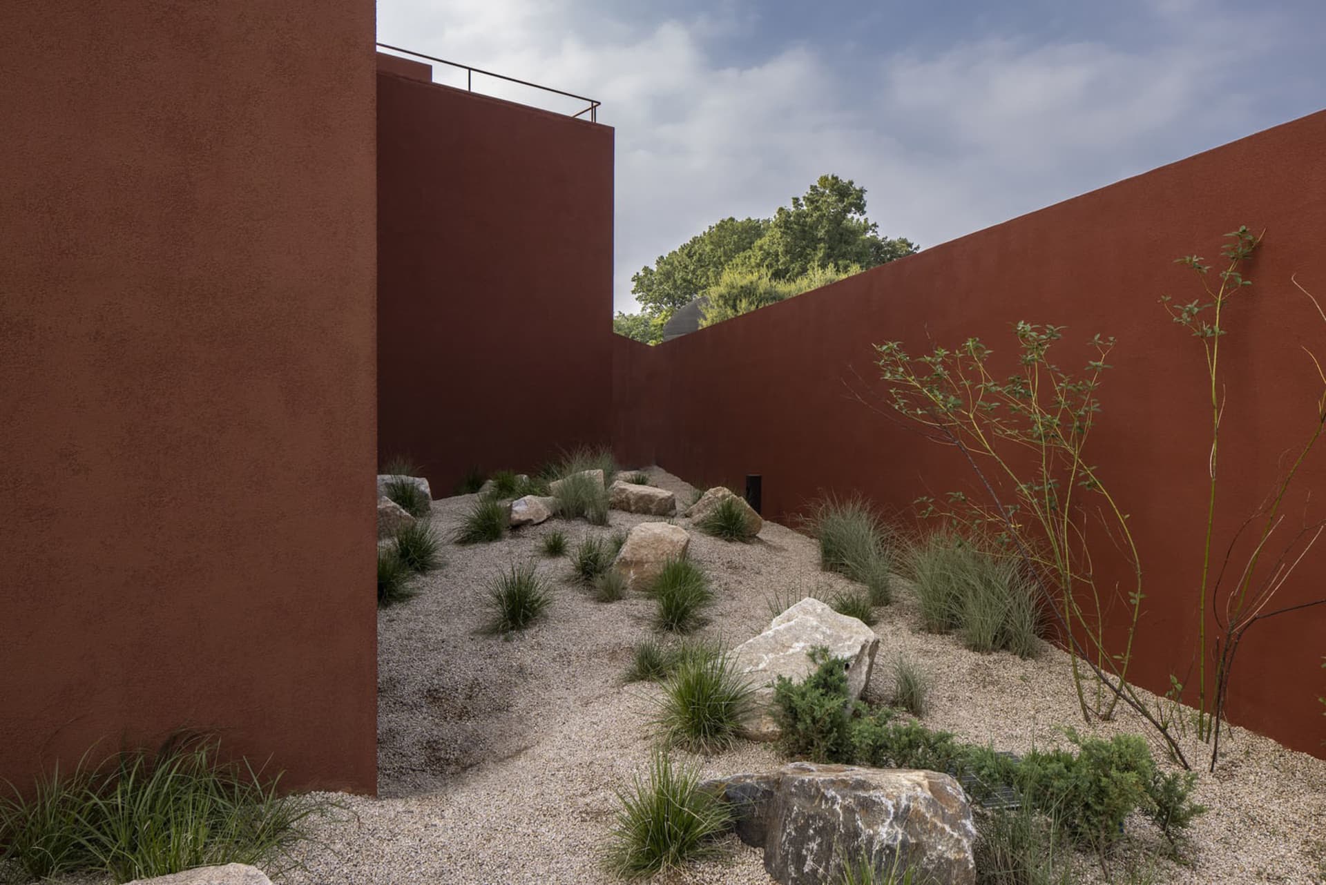 A serene outdoor courtyard with a red brick wall, stone walkway, and natural ambiance, surrounded by rocks and daylight