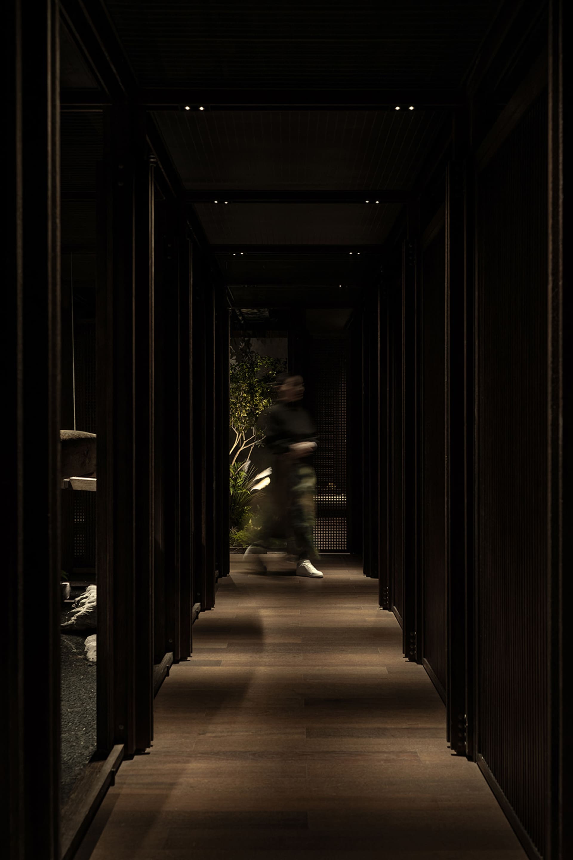 A hallway with wooden floors and walls, featuring two people walking and engaged in conversation