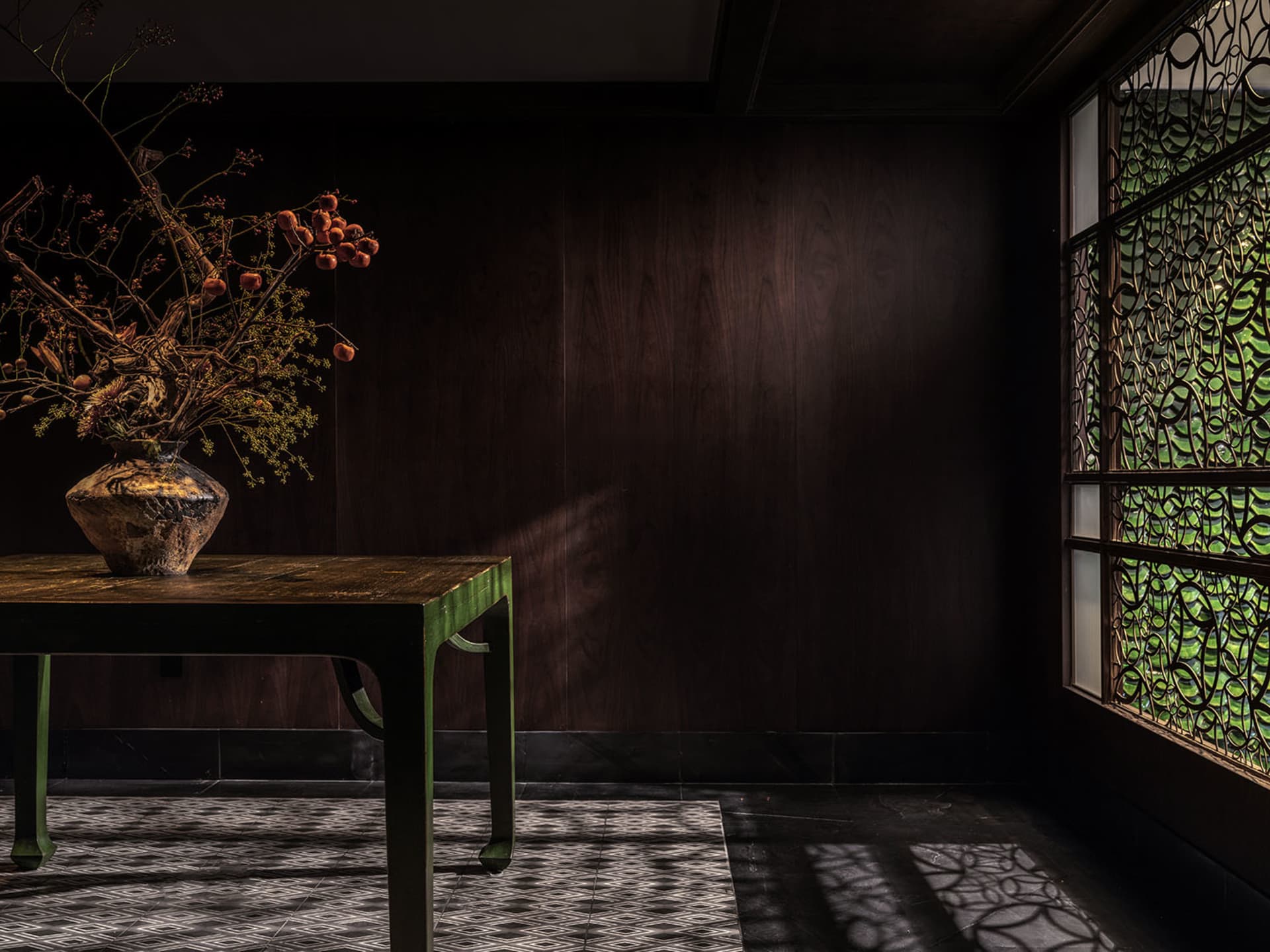 Cozy living room with a wooden table, brown walls, and a vase of flowers, featuring two chairs and a warm atmosphere