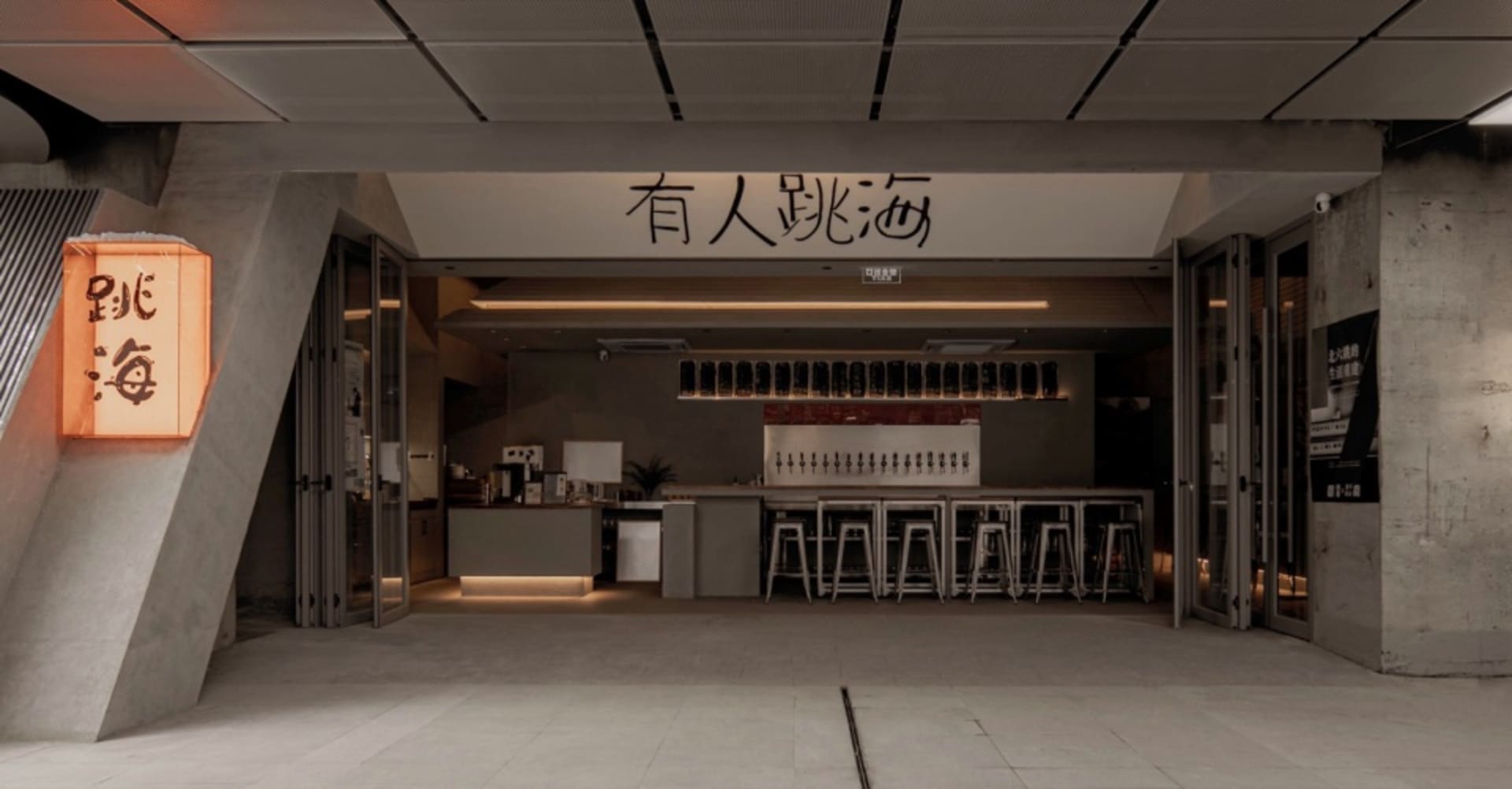 現代酒吧區，灰色檯面搭配高腳椅與桌椅，周圍環繞酒瓶，適合社交聚會