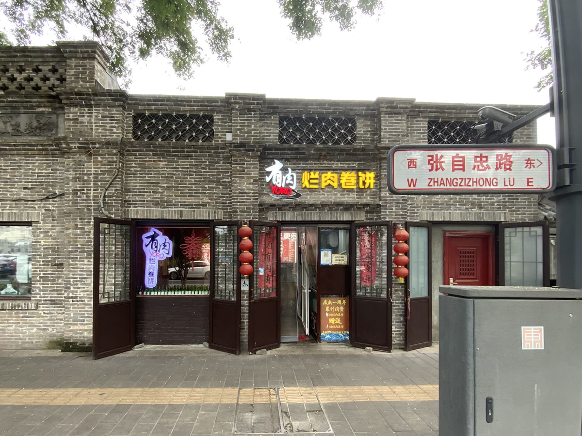 A warm and inviting Asian restaurant with a brick exterior, wooden doors, and red accents, featuring tables and chairs arranged in a comfortable dining atmosphere