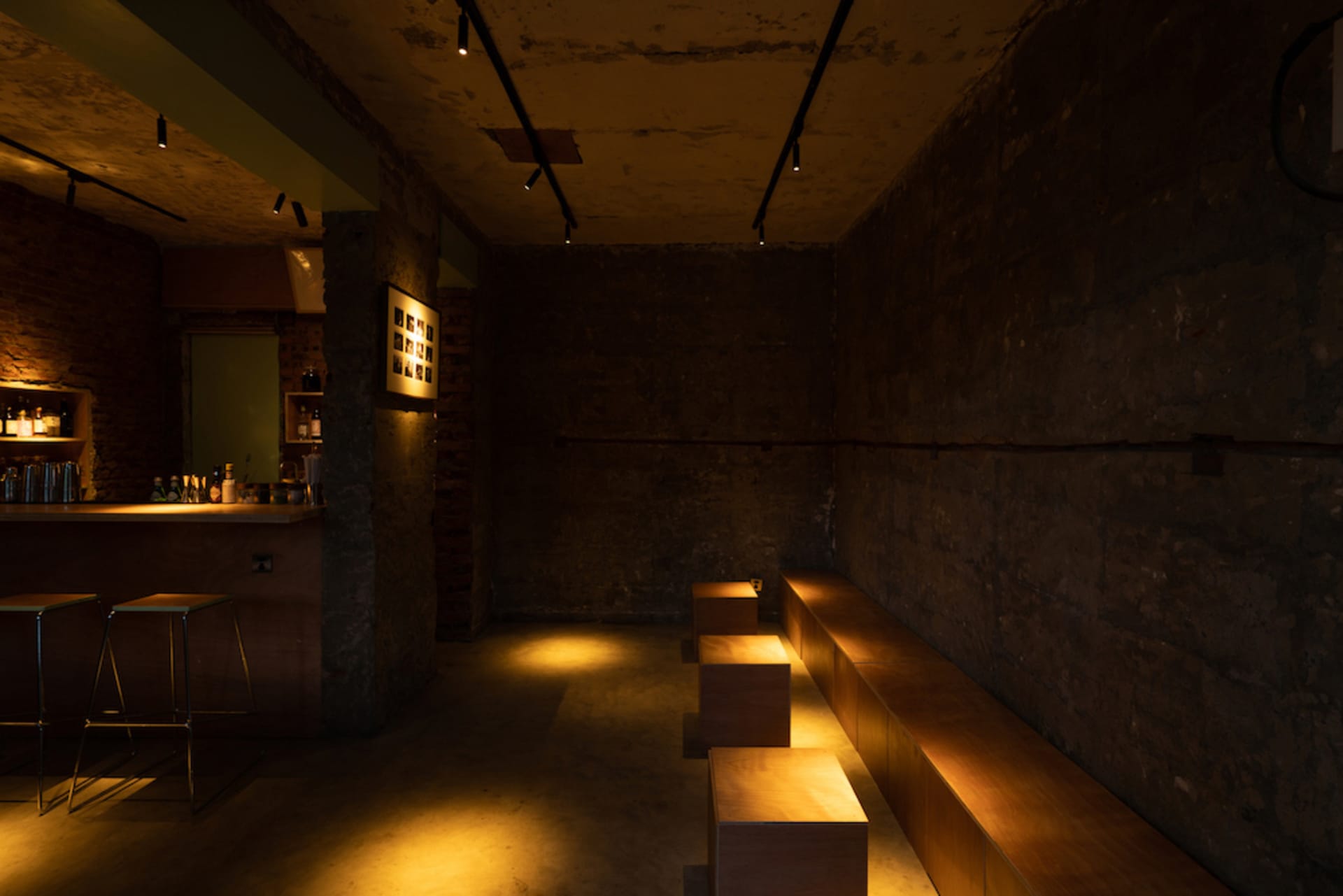 Empty room with a concrete floor, a bar area with a counter and bench, and several bottles on the counter, giving an impression of neglect