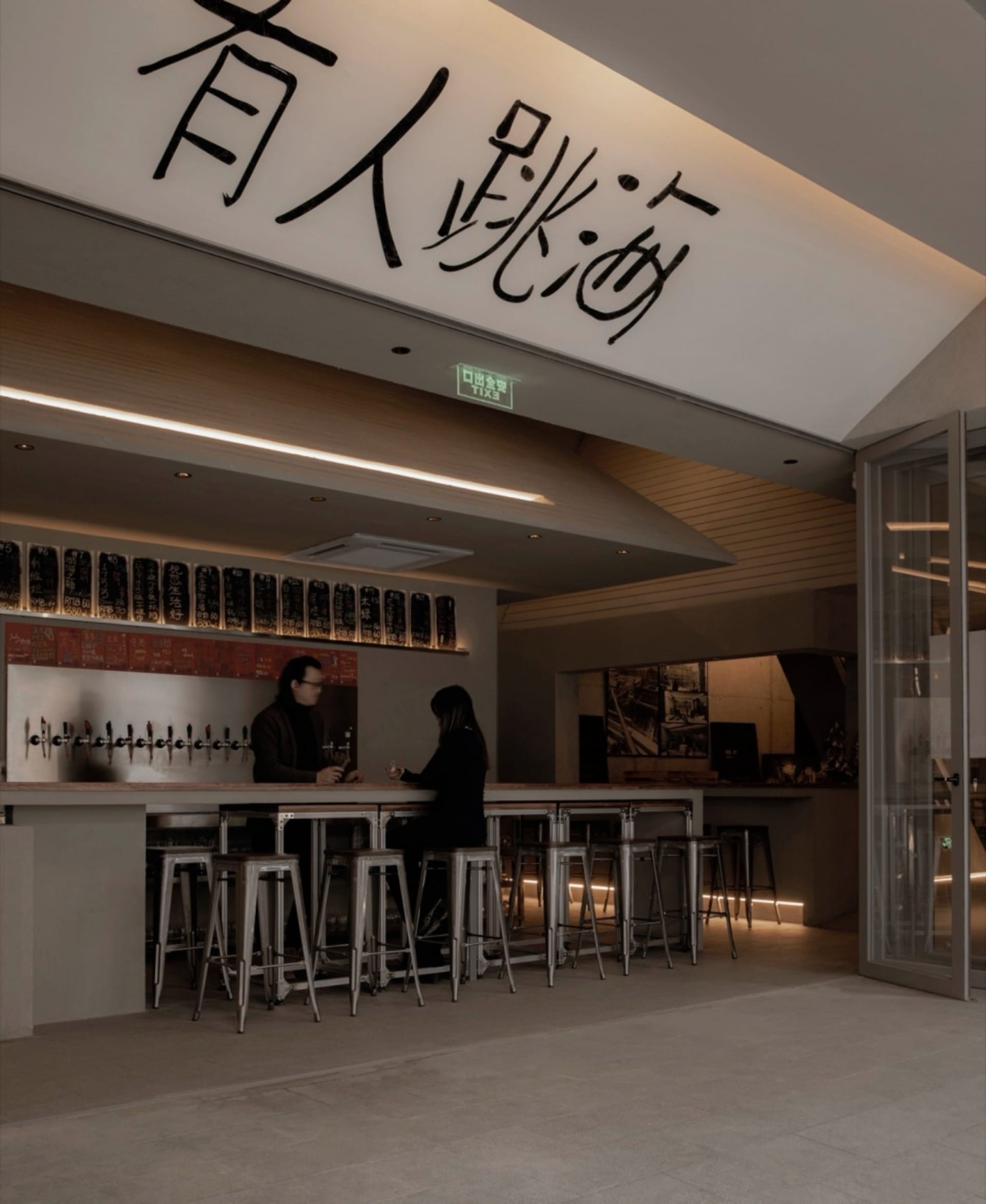 Casual modern restaurant with a bar featuring stools and tables, bottles on display, and a contemporary design