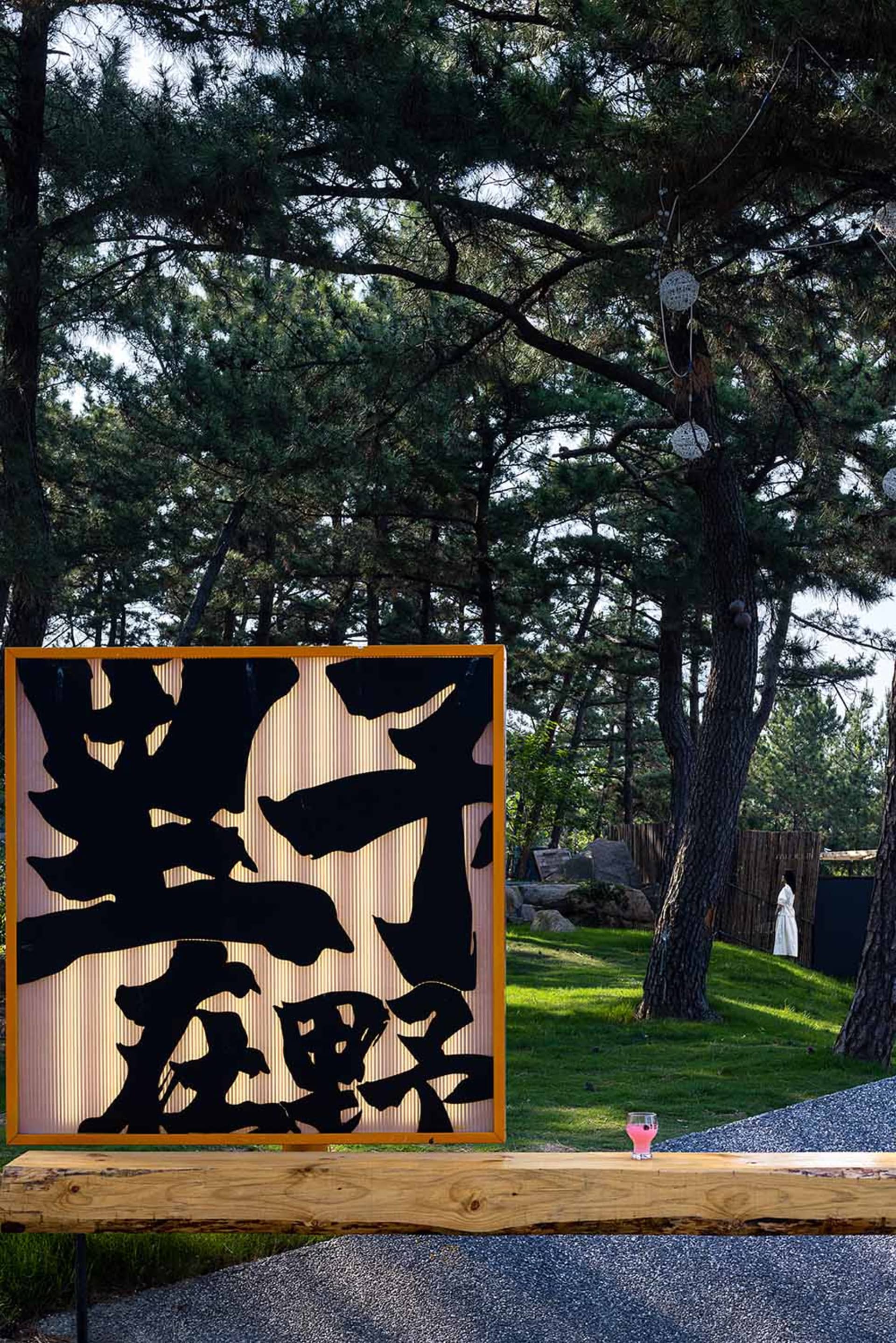 A serene Asian garden with a woman standing in front of a wooden fence, surrounded by trees and a peaceful atmosphere