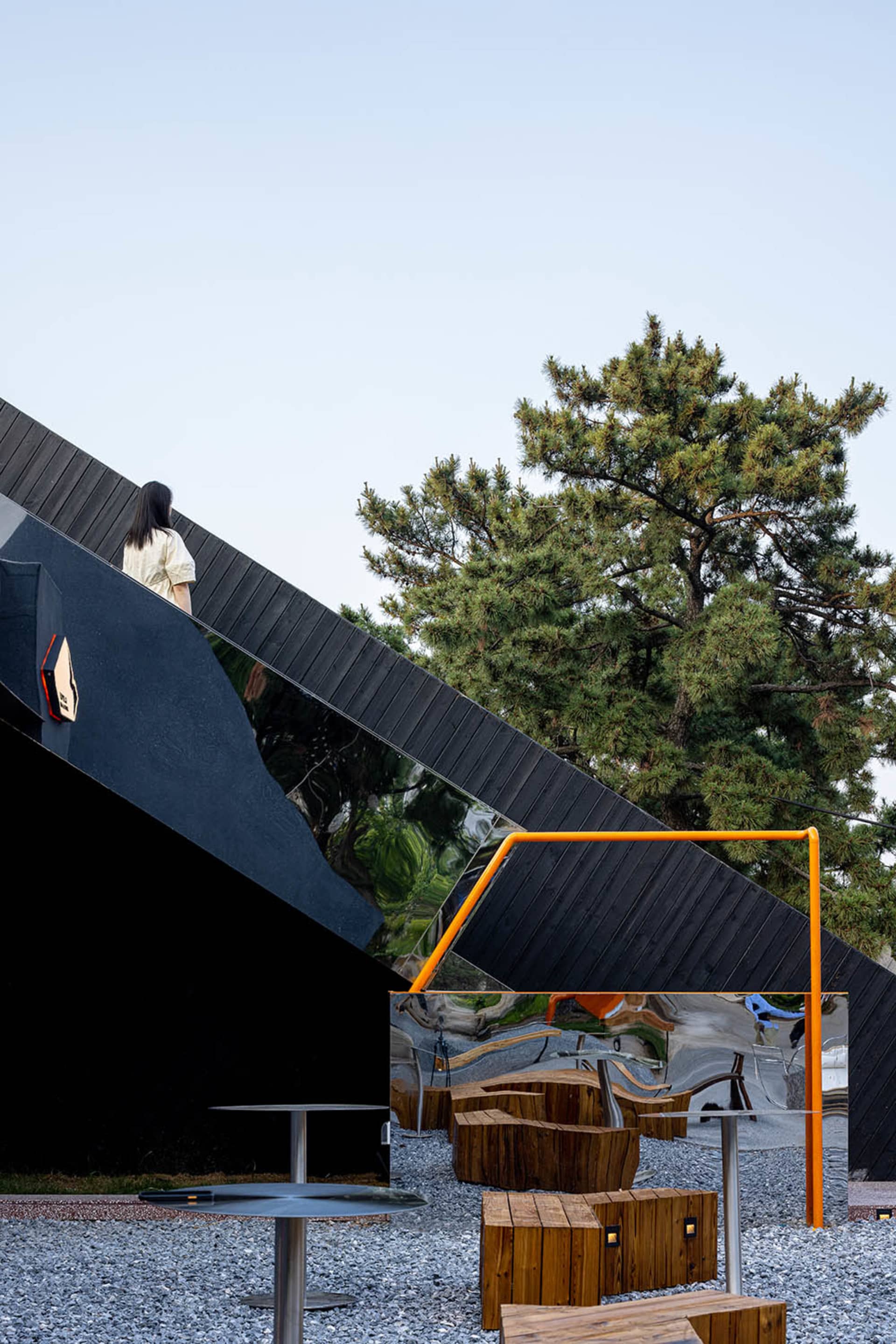 A woman stands on a balcony with a black railing, surrounded by trees in a residential area with a modern design