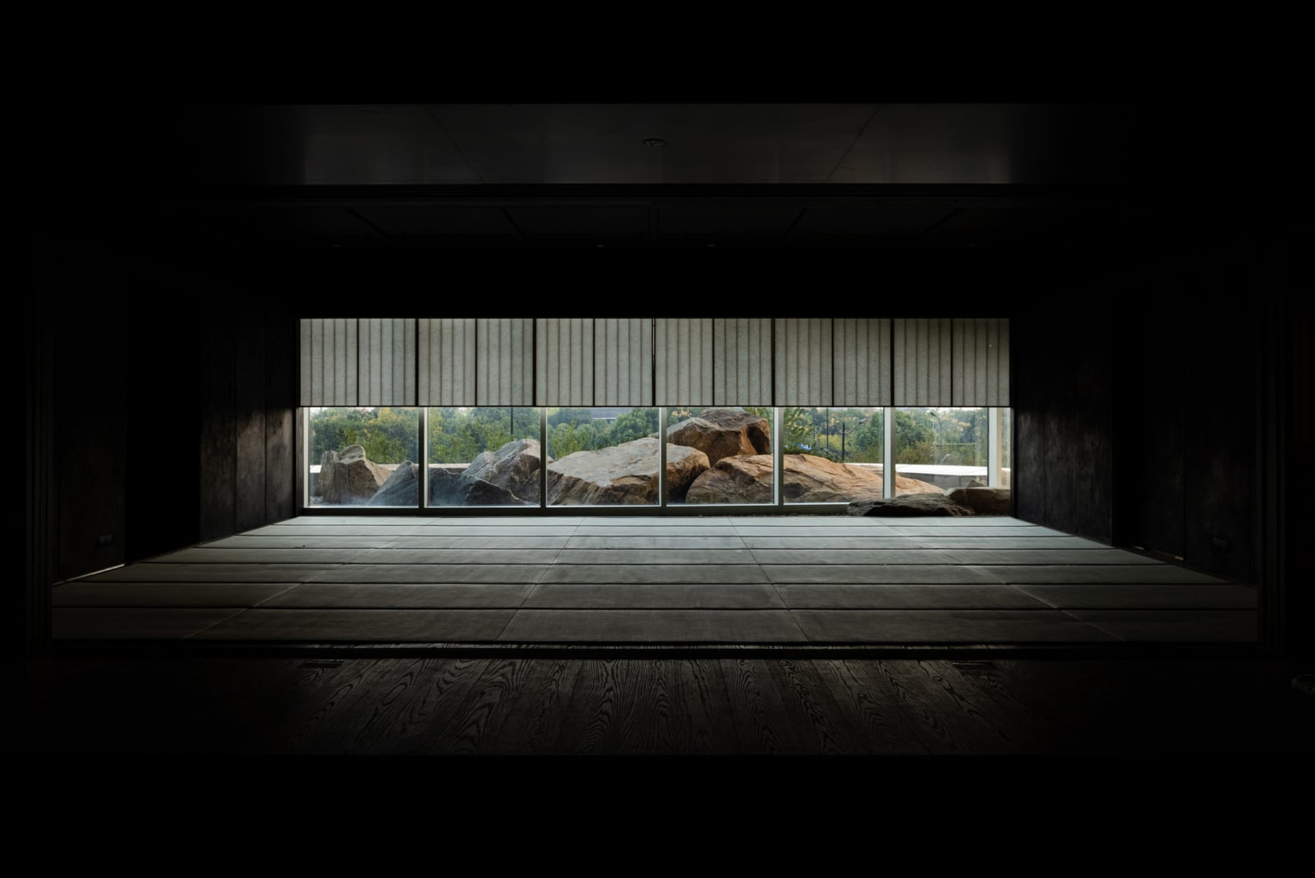 An empty room with large windows, natural light, and several rocks arranged within the space