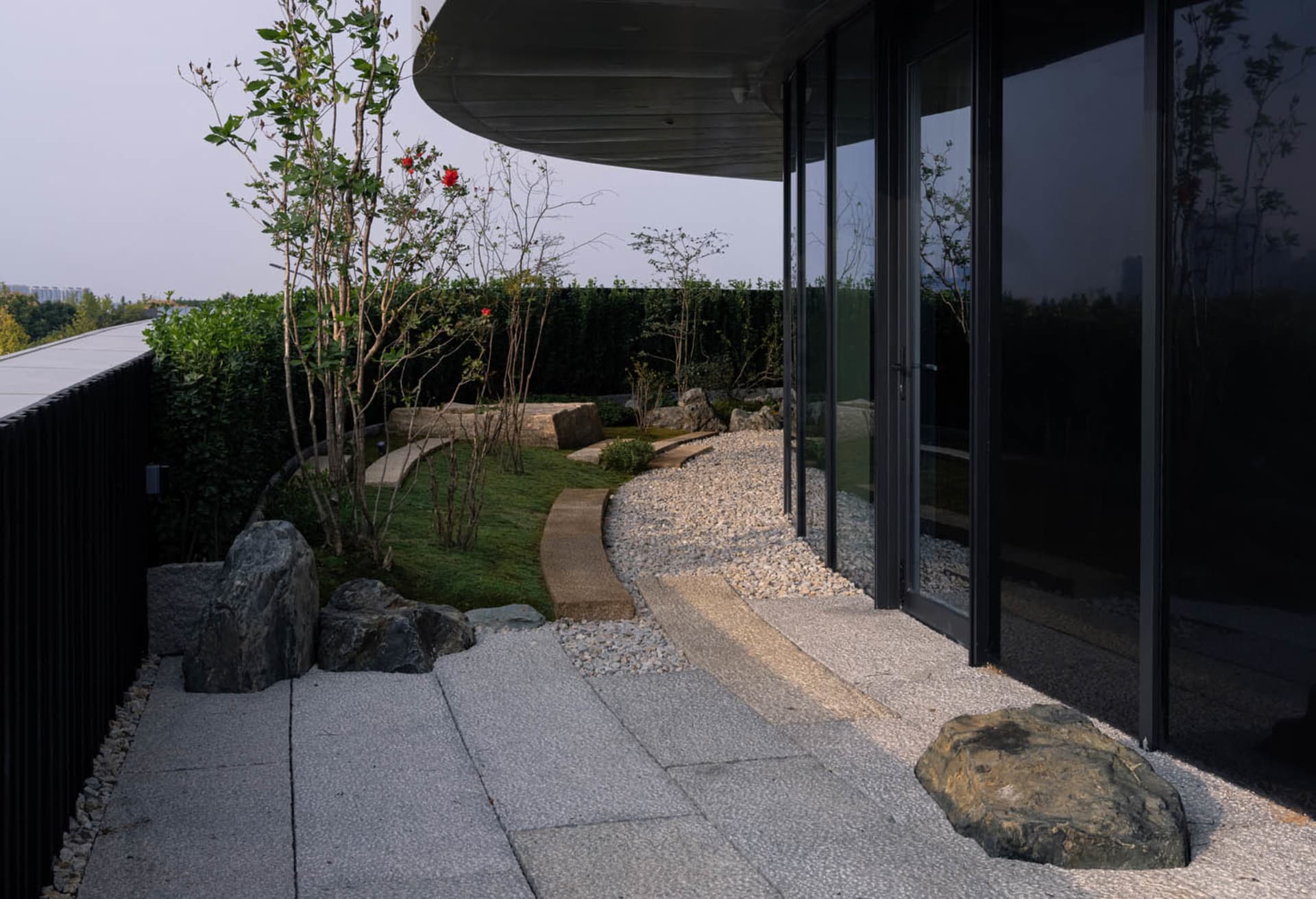 A modern patio with a glass door, rock garden, small waterfall, and potted plants, creating a serene atmosphere with natural elements