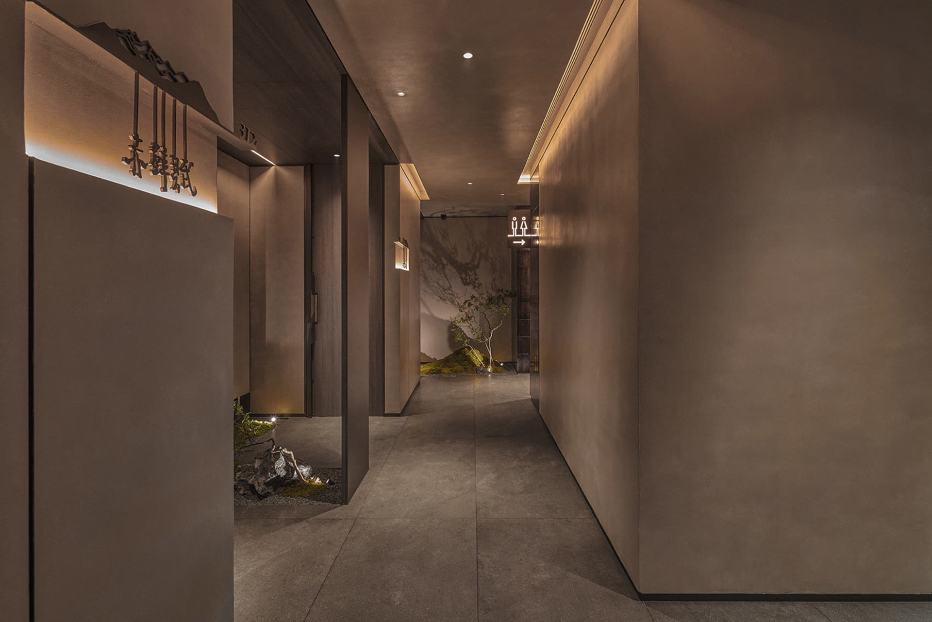 Empty grey stone hallway with a brown wooden door and two chandeliers providing illumination