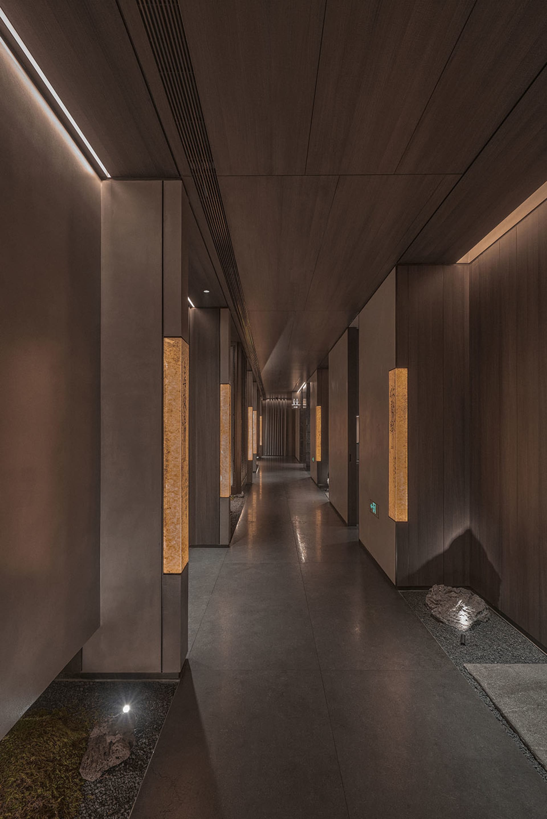 A calm and inviting empty hallway with a wooden floor and ample lighting from multiple fixtures on both sides