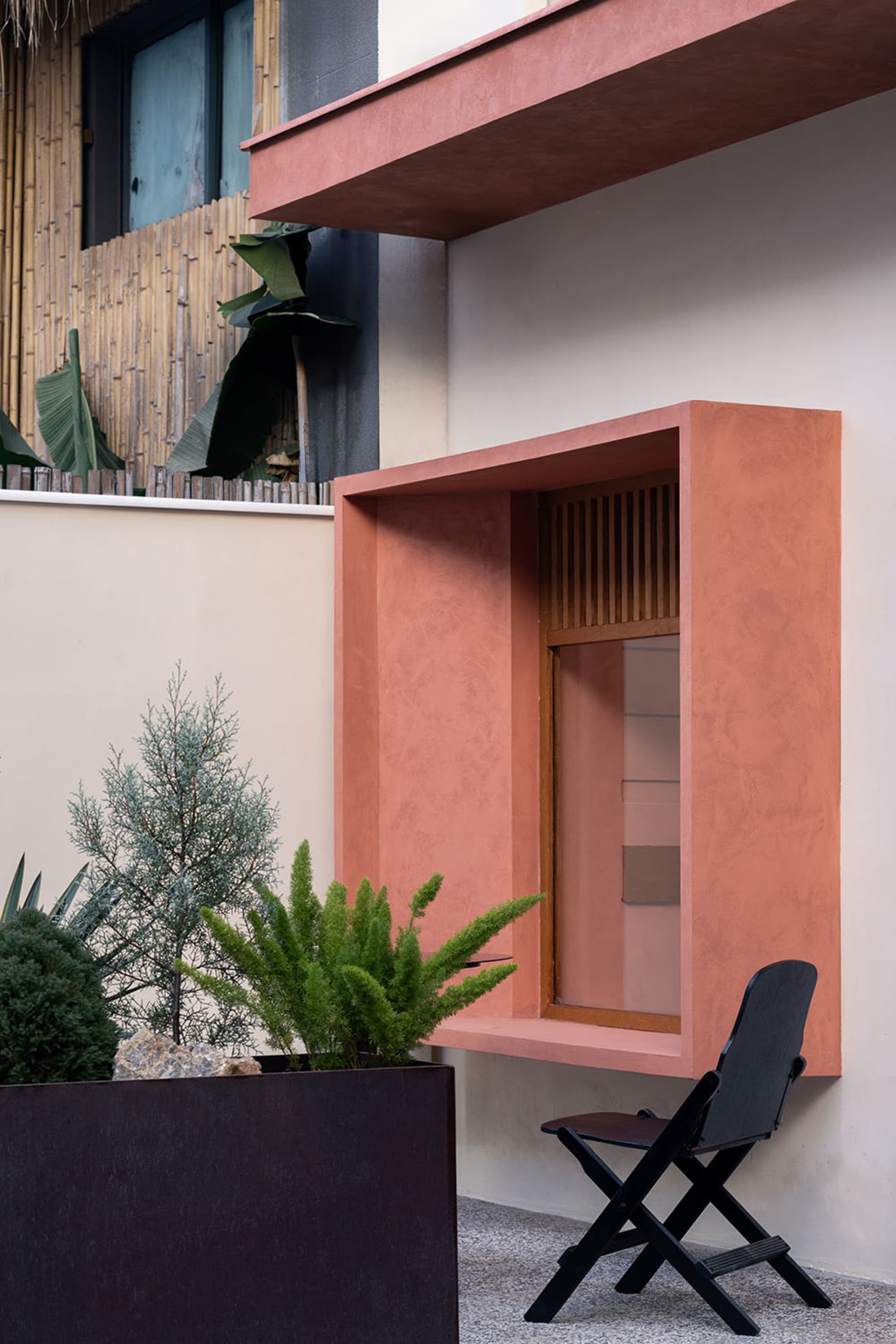 Cozy living space with a pink accent wall, a window, two chairs, a dining table, and several potted plants