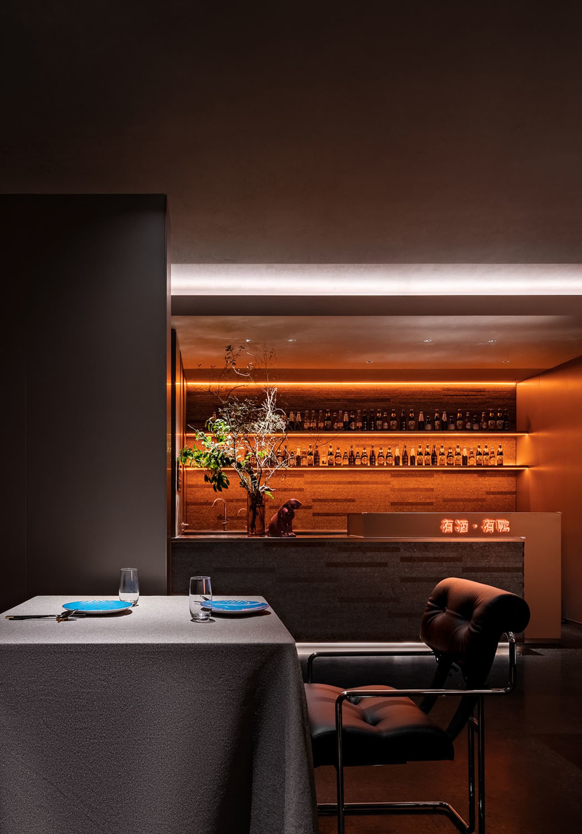 A cozy bar area in a restaurant with bottles, wine glasses, and a dining table in the background