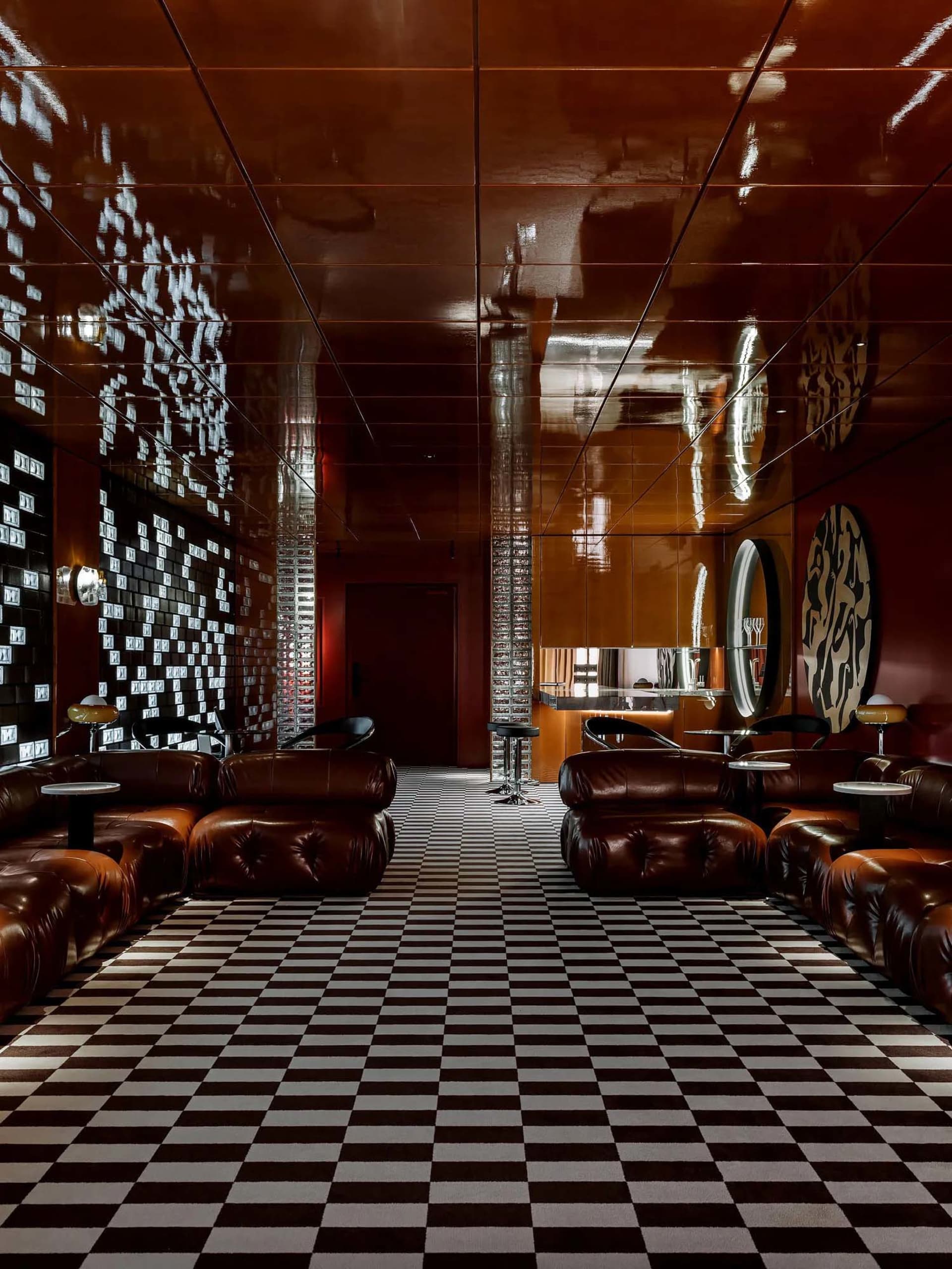 A modern living area with a checkered floor, leather chairs, and a mix of wood and metal materials, featuring warm lighting and a comfortable atmosphere