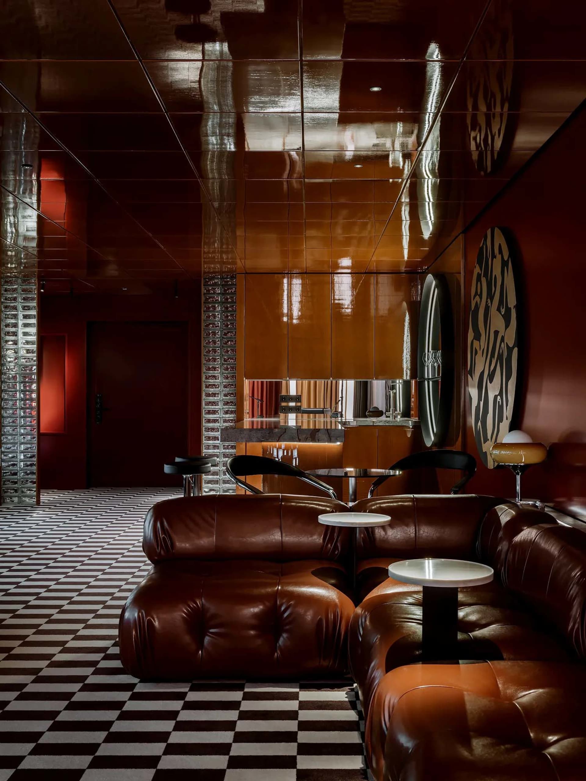 A warm and inviting living space with red walls, brown leather couches, and comfortable seating options, including chairs and dining tables, with wine glasses scattered throughout