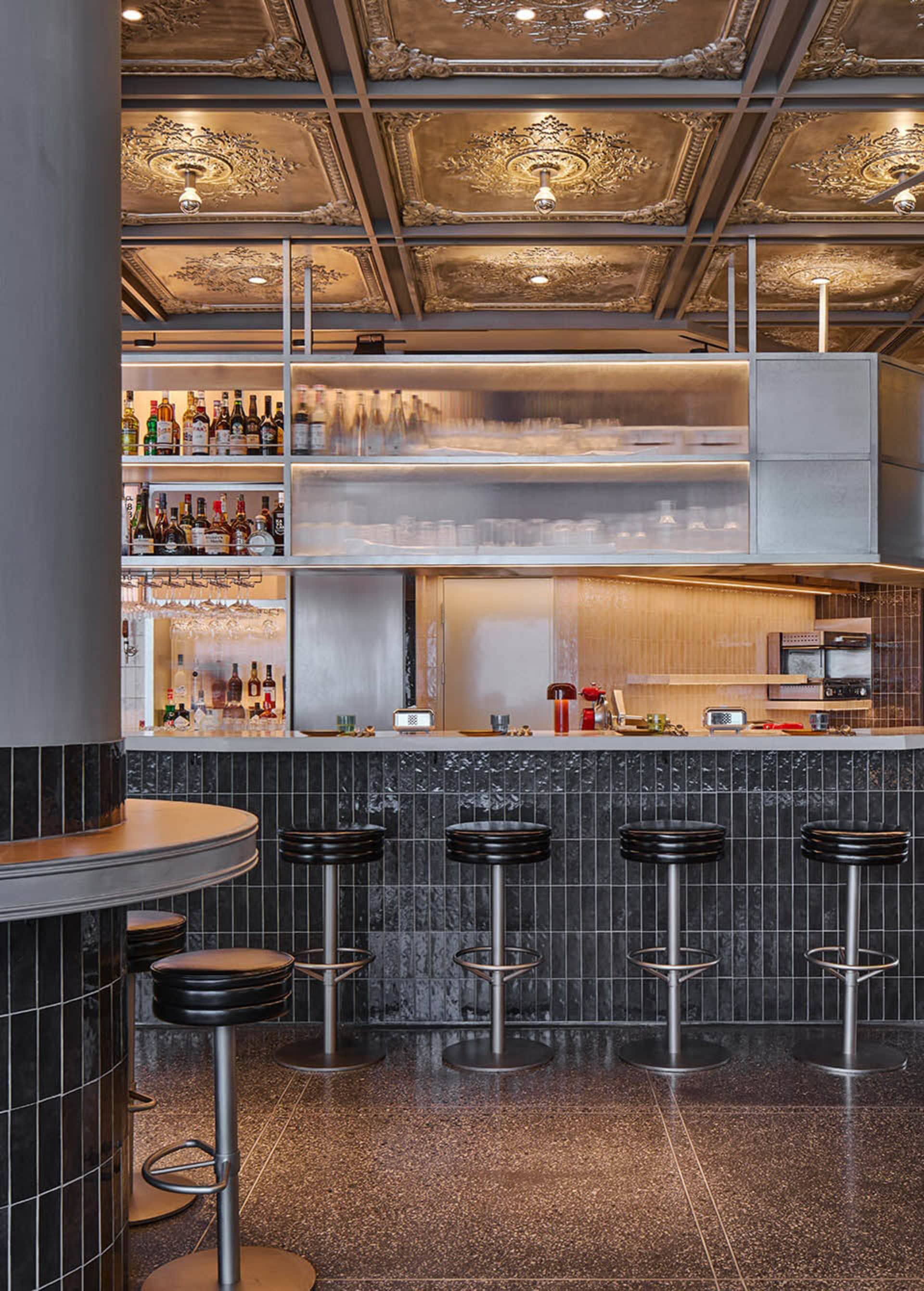 A cozy bar area with a long wooden counter and stools, surrounded by bottles and an inviting atmosphere