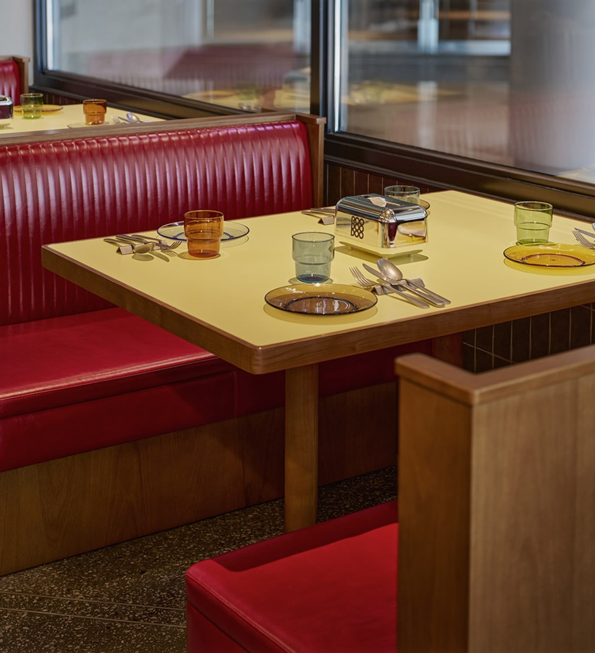 Cozy dining space with a yellow table surrounded by red benches, featuring various tableware and wine glasses